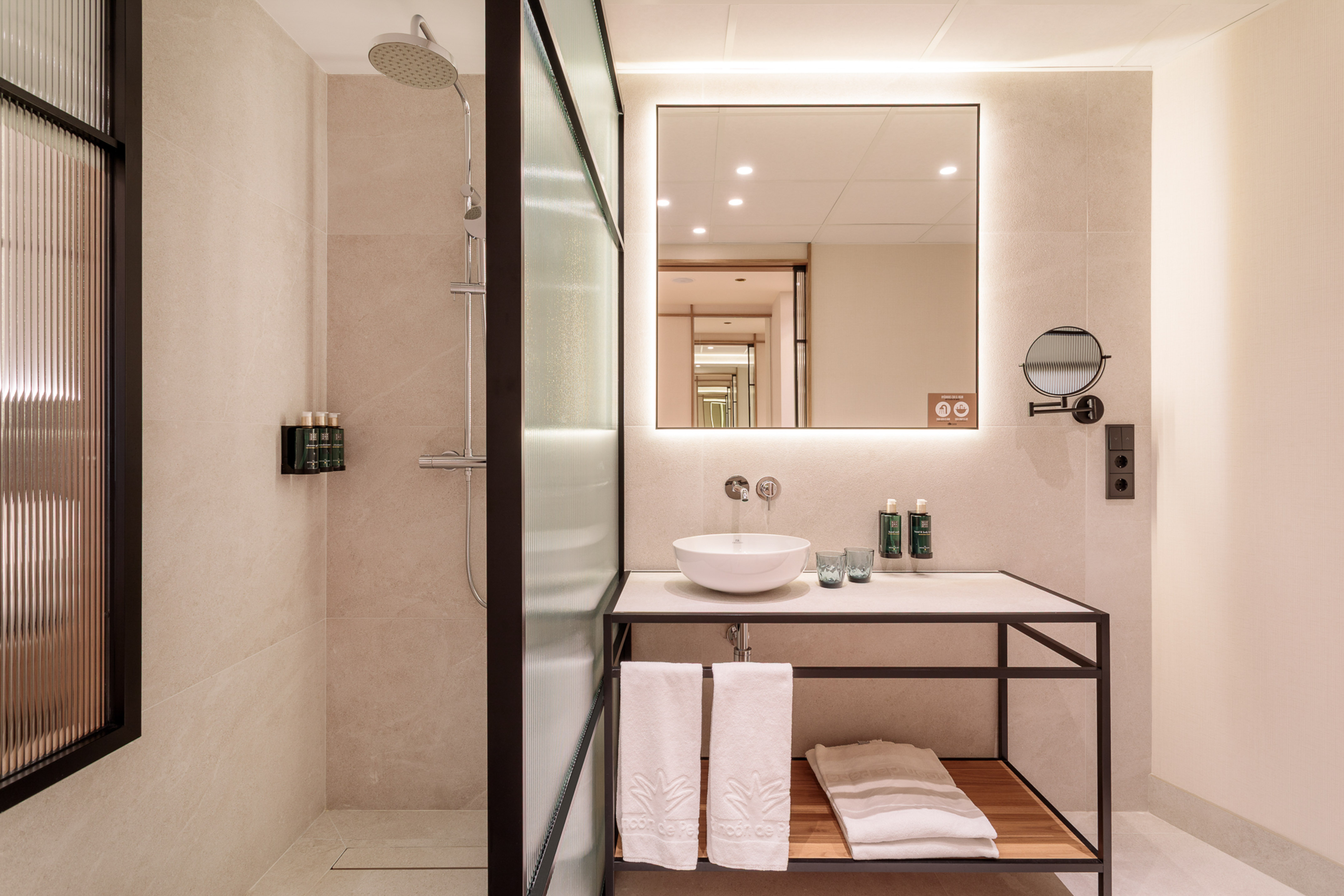 Modern hotel bathroom with glass shower, basin vanity, and lighted mirror.