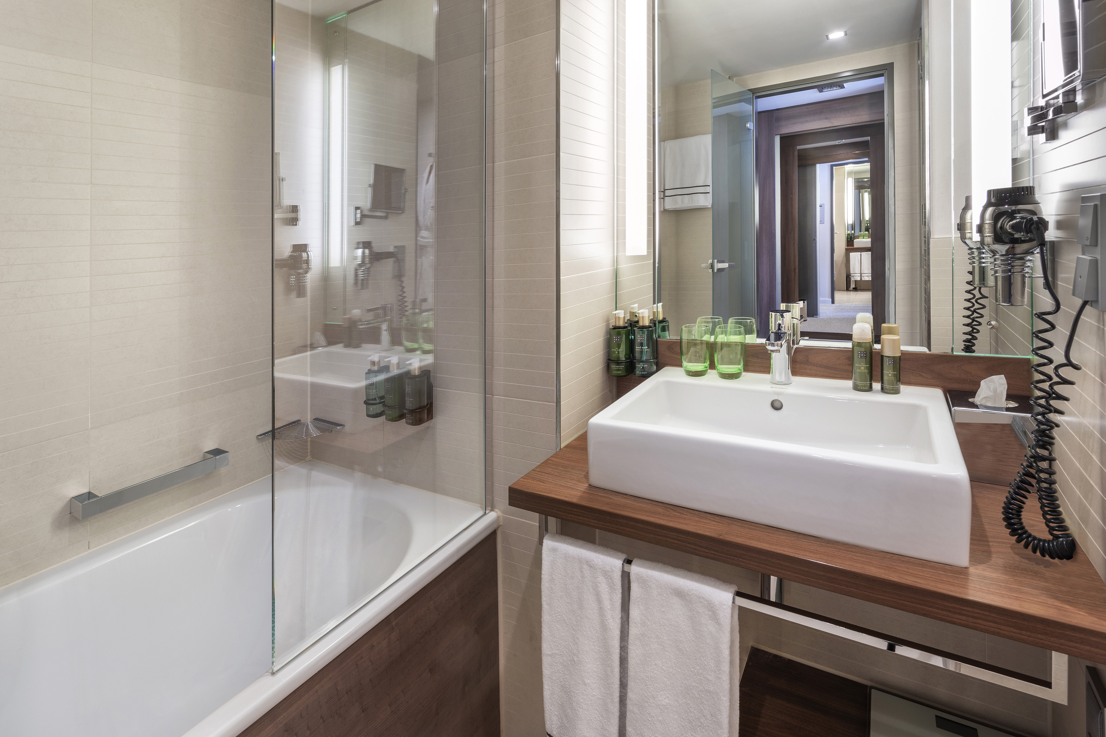 Modern bathroom with white vessel sink, wood vanity, bathtub, and mirror.
