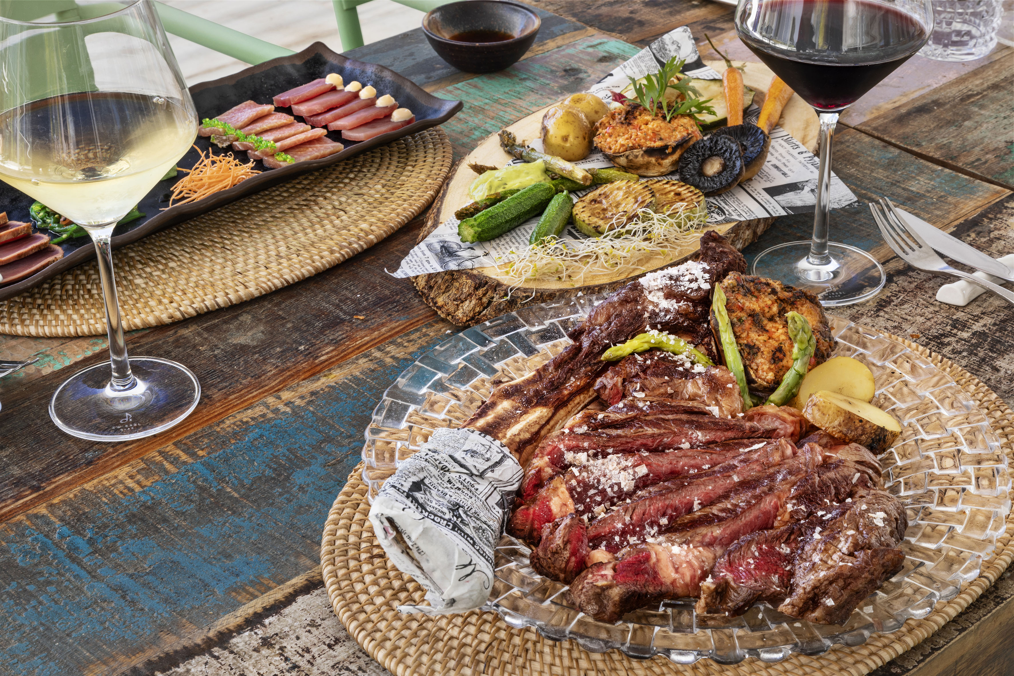 Sliced steak, grilled vegetables, seared tuna, and wine on a rustic table.