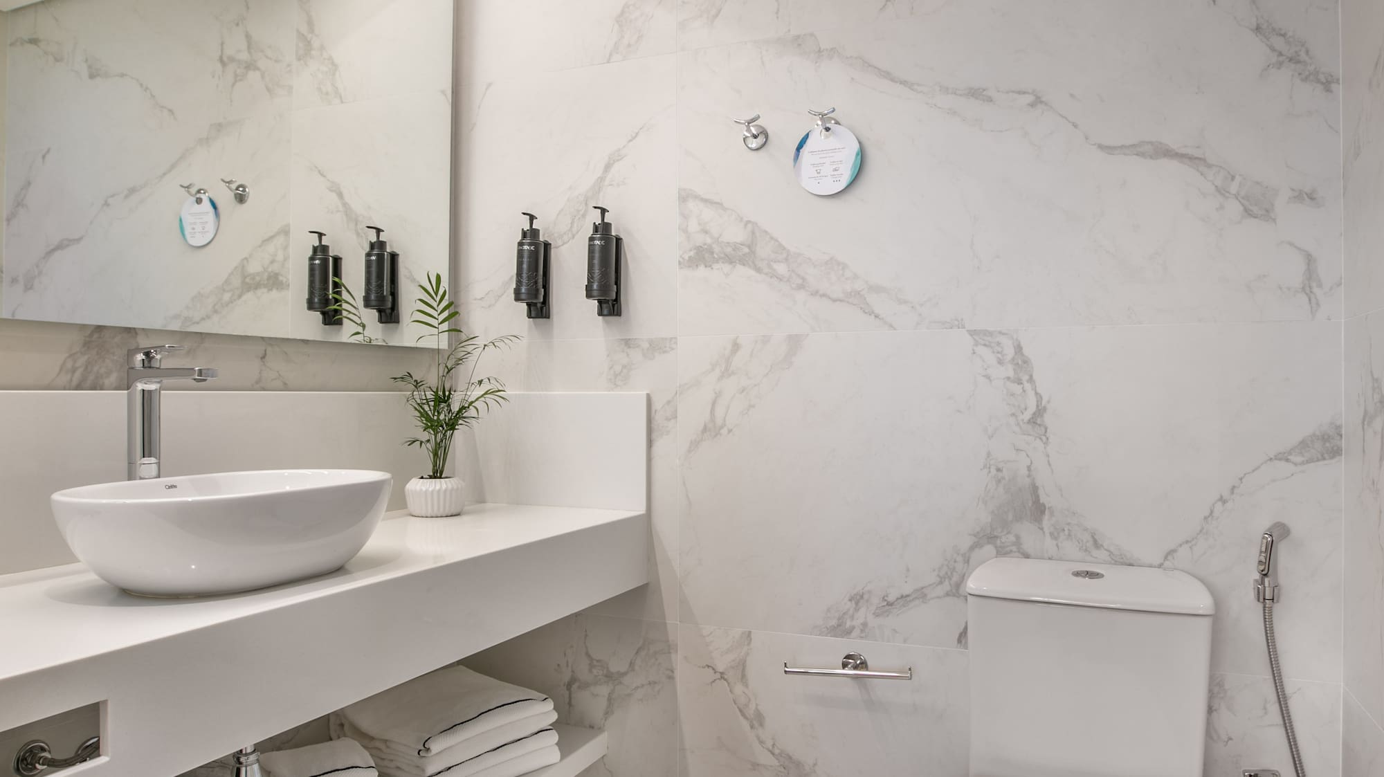 Modern white marble bathroom with basin, toilet, mirror, and linear LED lighting.