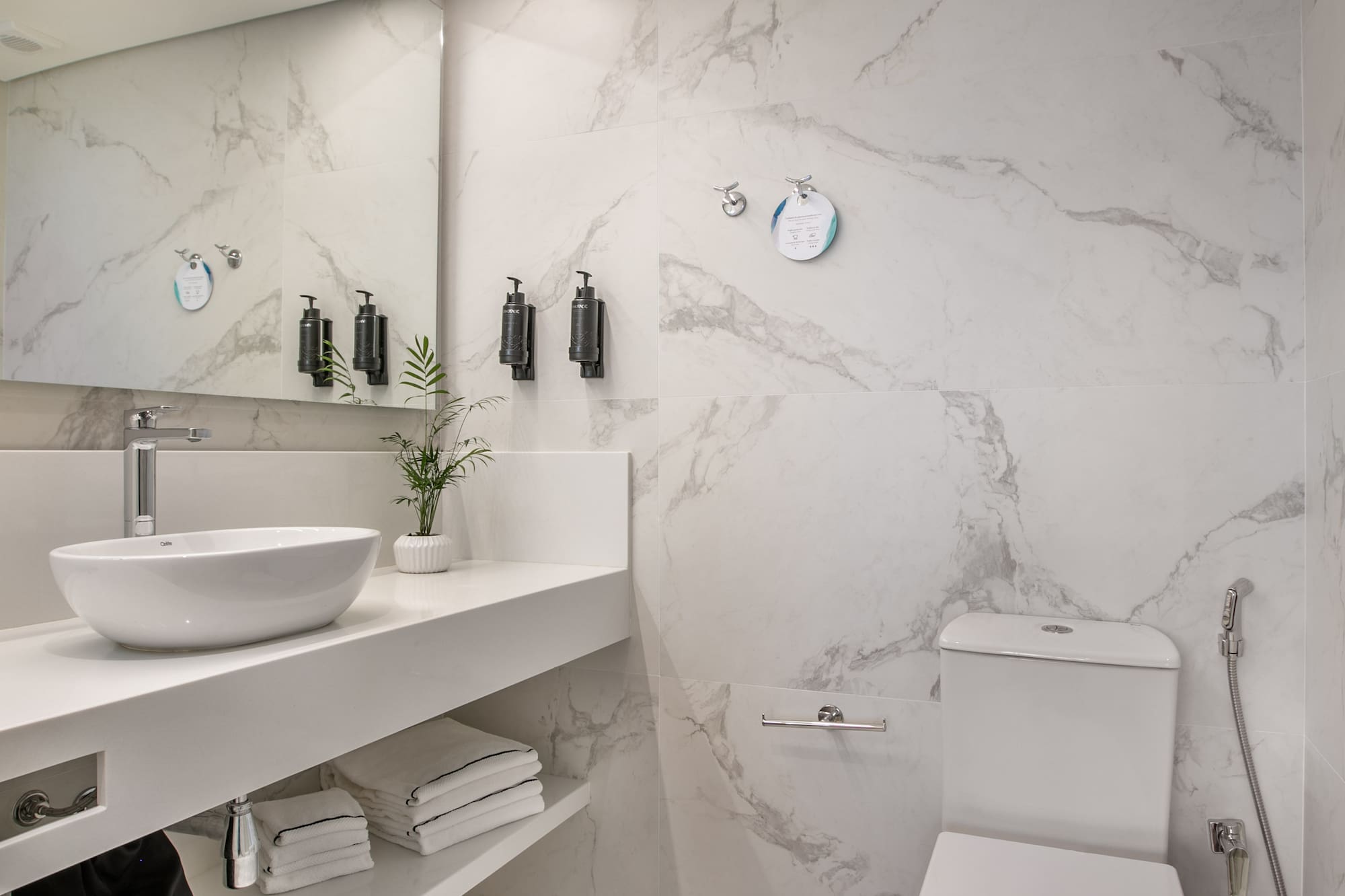 Modern white marble bathroom with basin, toilet, mirror, and linear LED lighting.