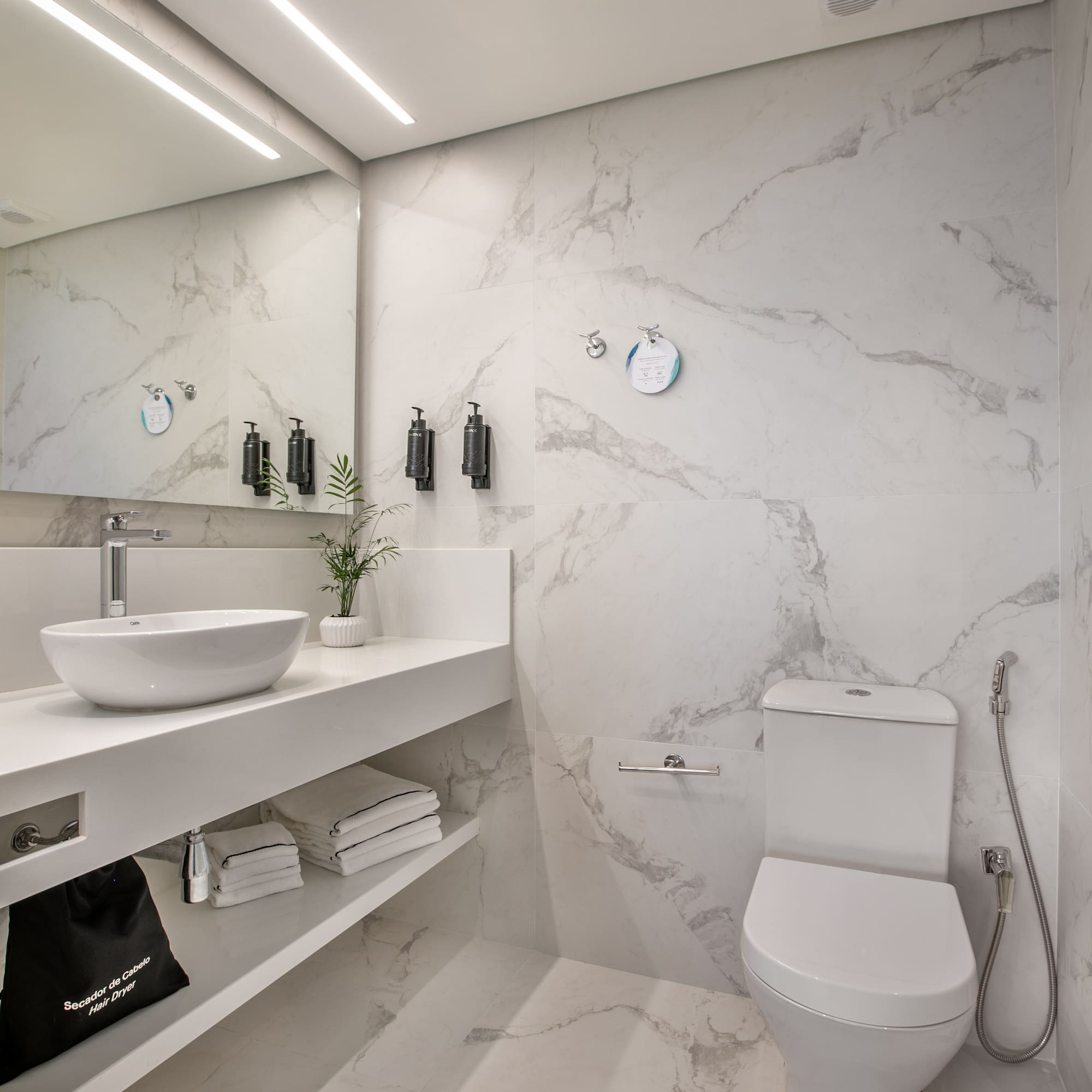 Modern marble bathroom with white vanity, sink, toilet, and bright LED lighting.