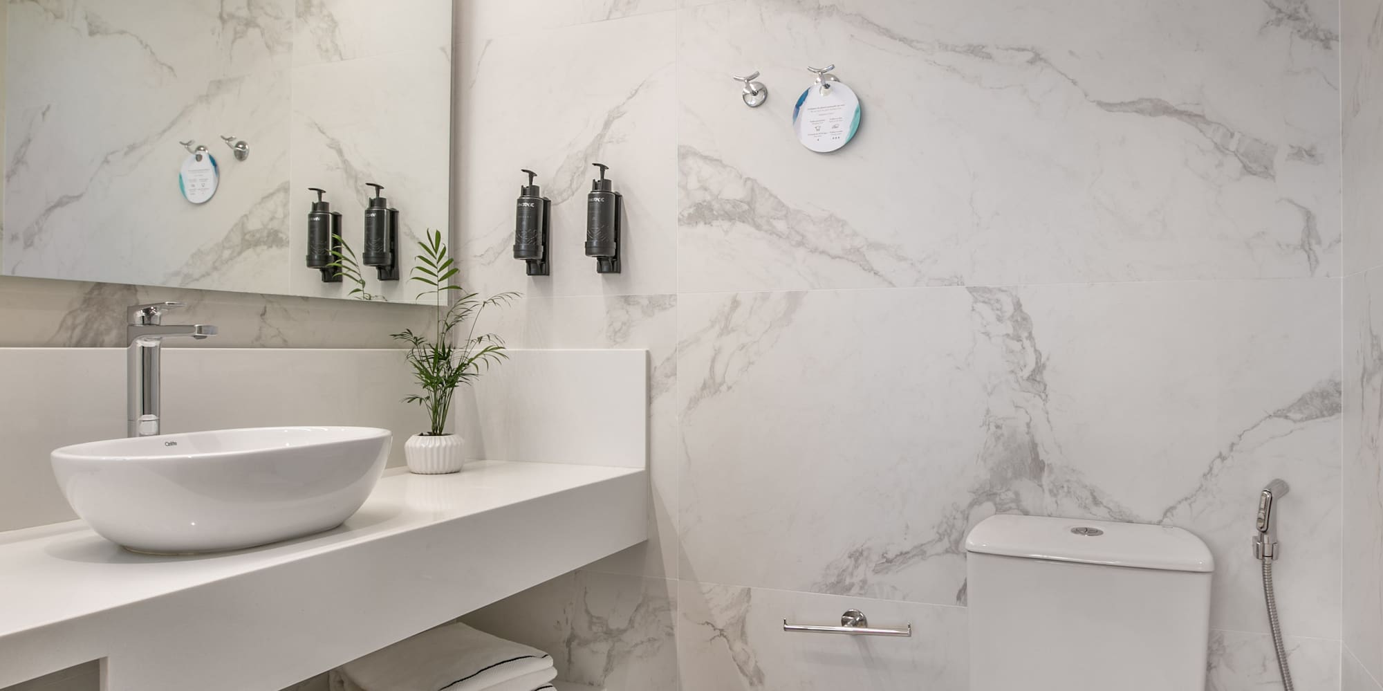 Modern marble bathroom with white vanity, sink, toilet, and bright LED lighting.