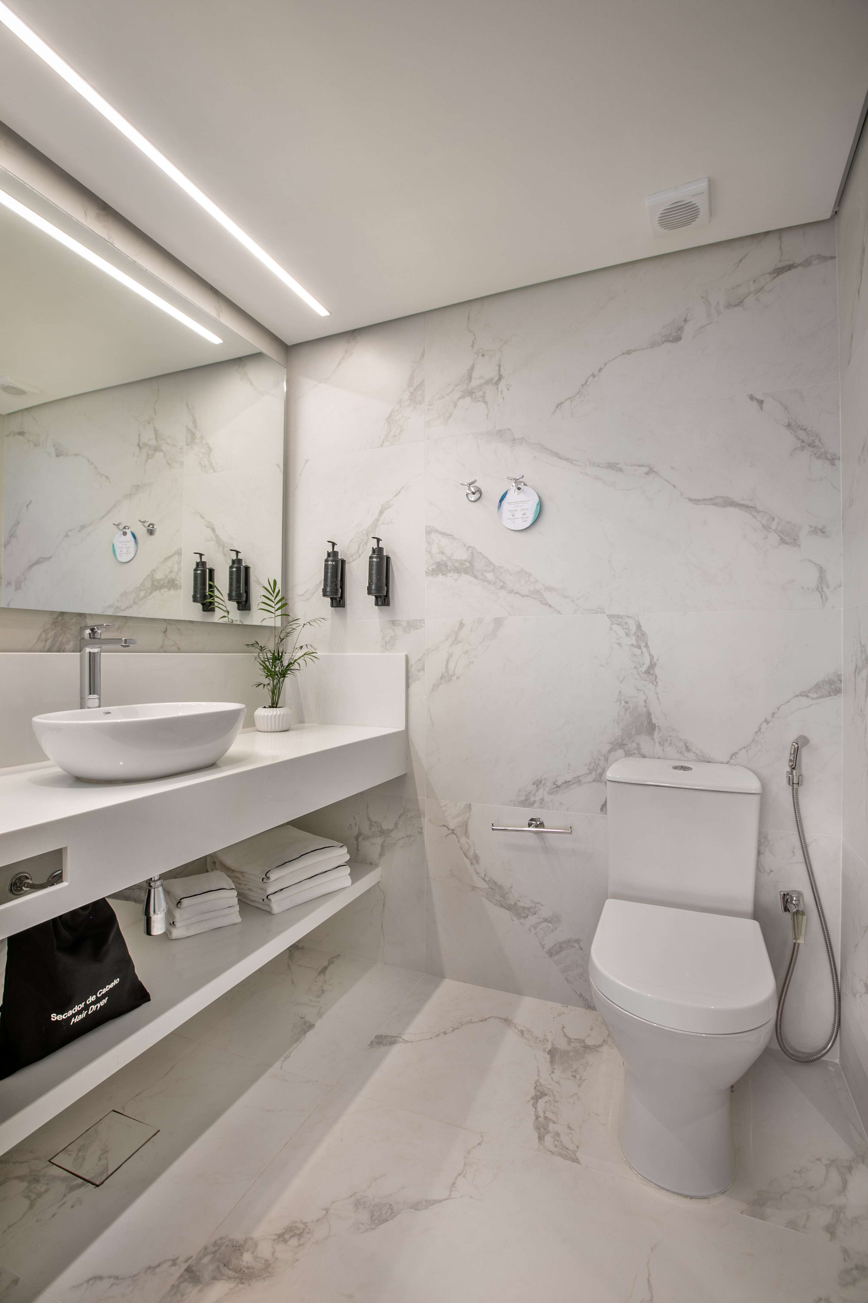 Modern white marble bathroom with basin, toilet, mirror, and linear LED lighting.