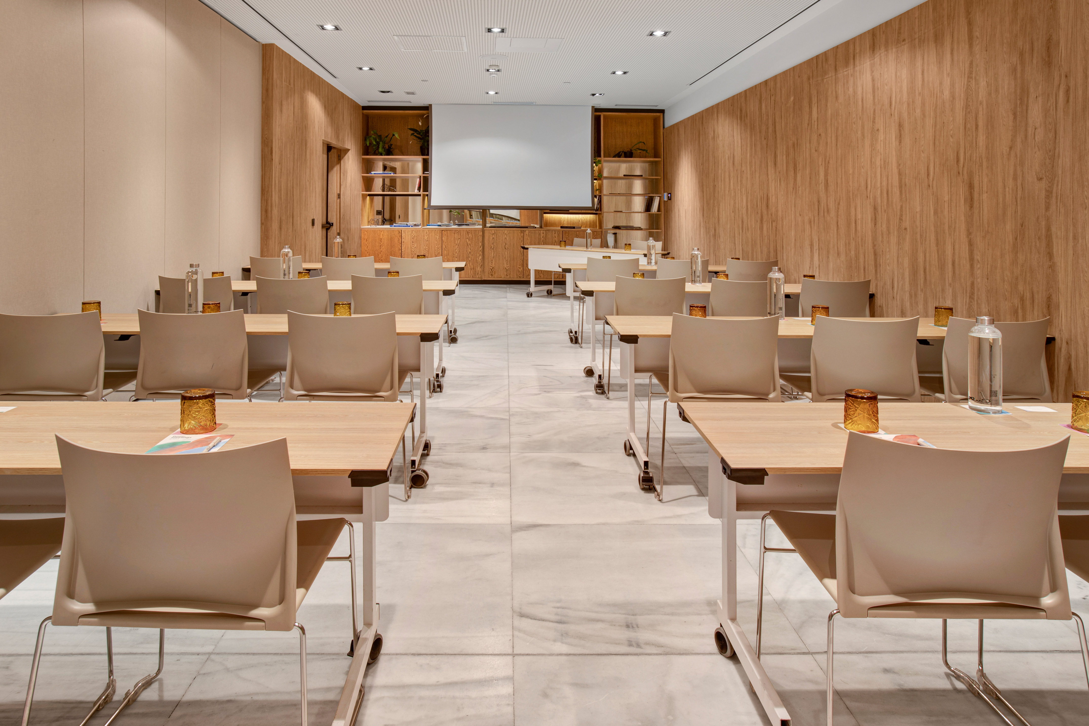 Modern conference room with tables, chairs, wood walls, and projection screen.