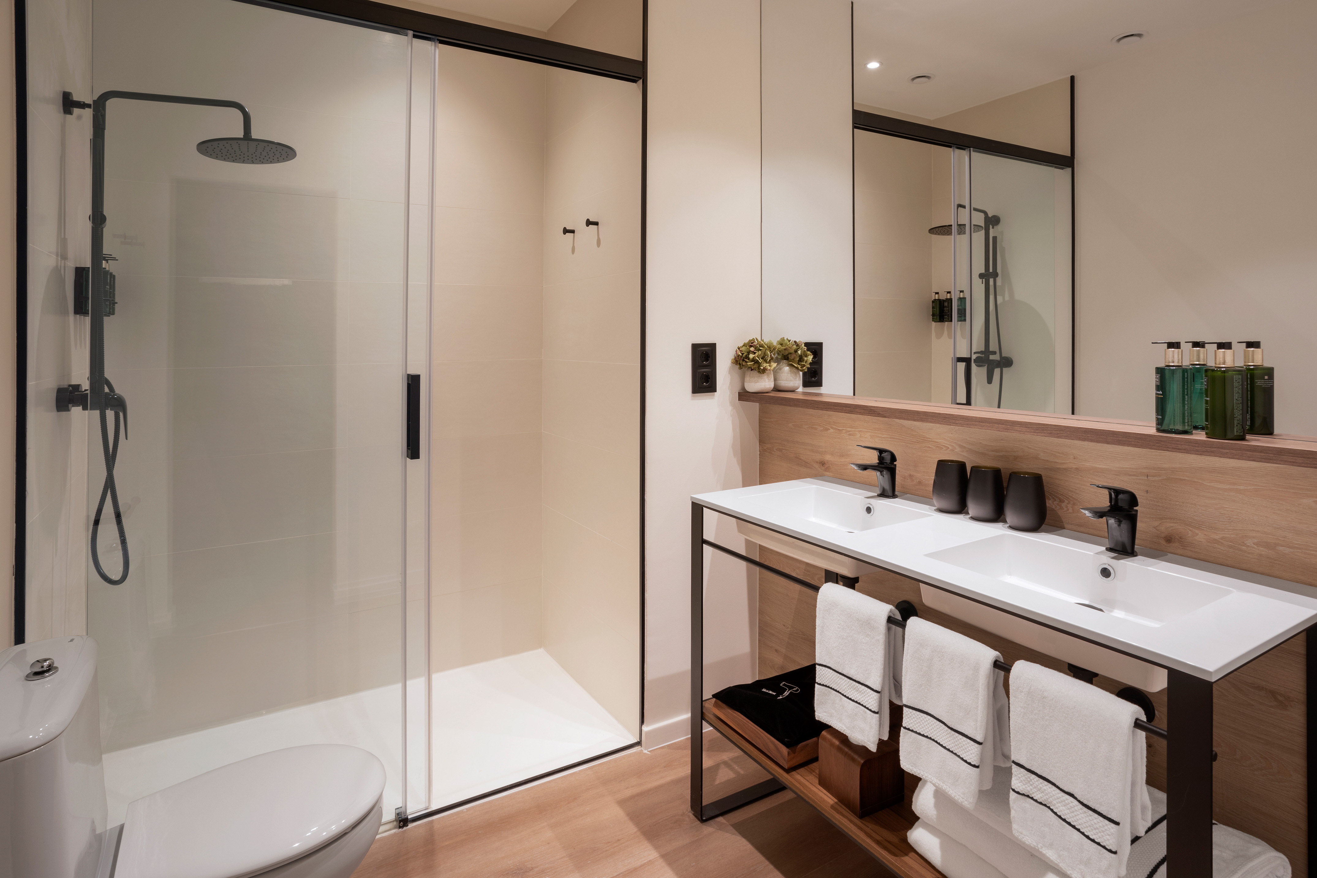 Modern bathroom with walk-in shower, dual sinks, black fixtures, and wood accents.