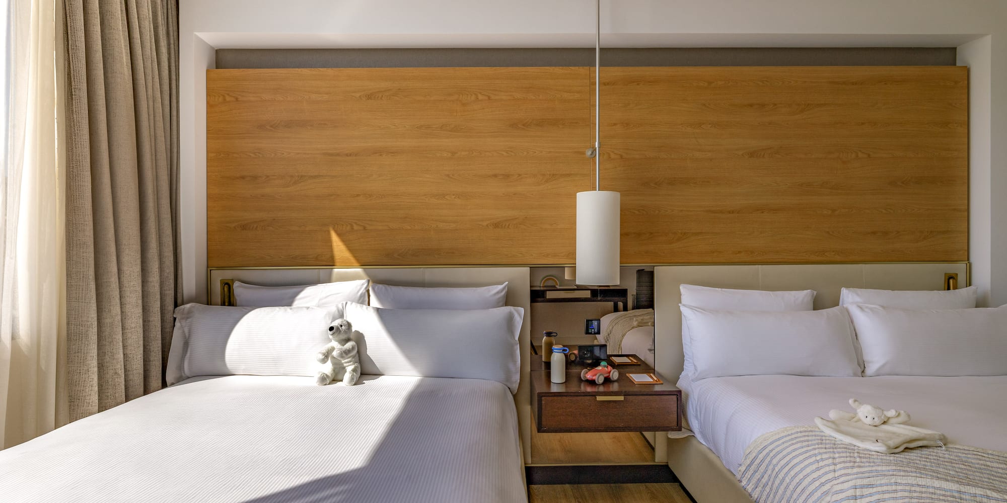 Modern hotel room with two beds, wood headboard, and kids' toys.