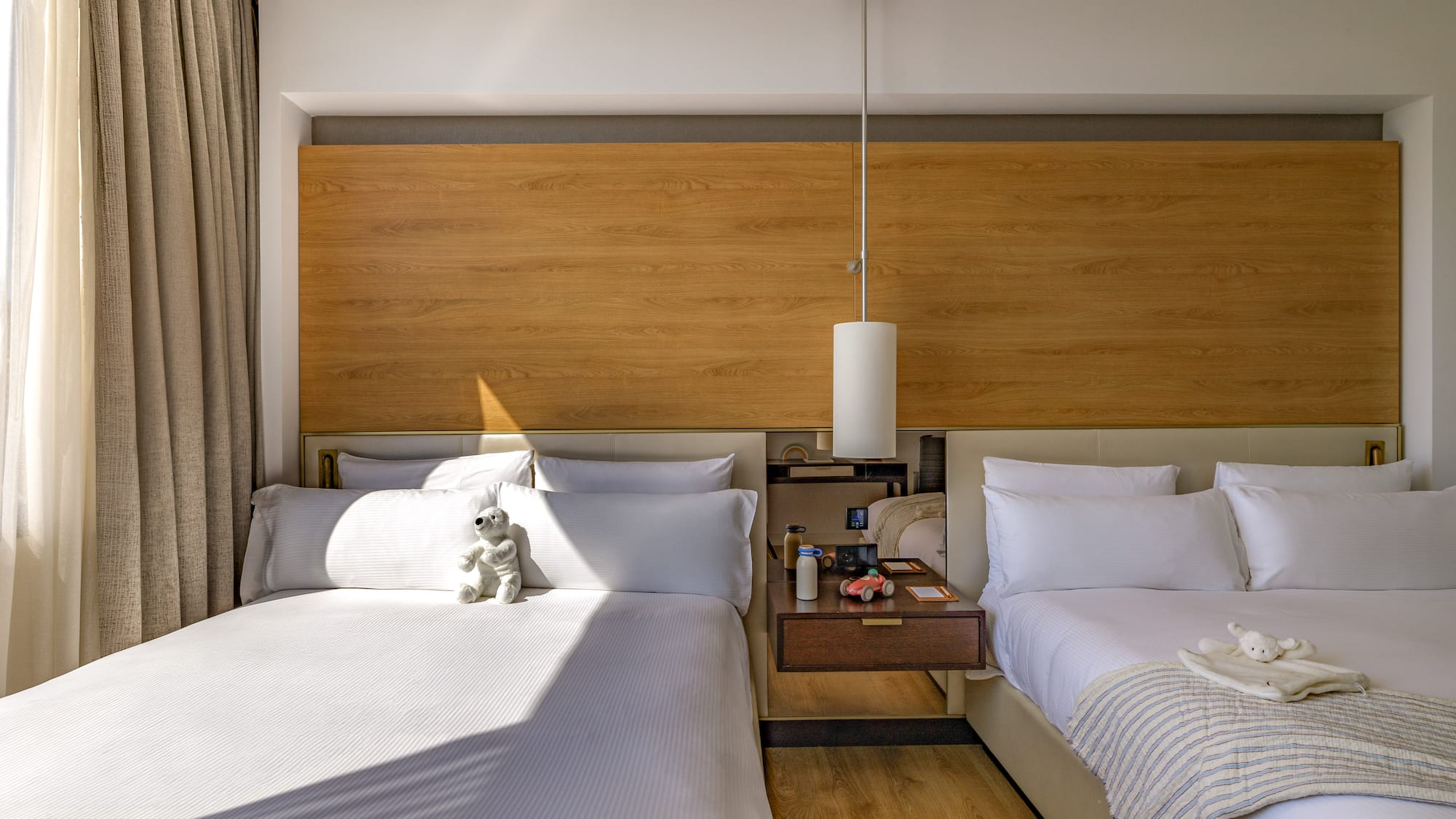 Modern hotel room with two beds, wood headboard, and kids' toys.