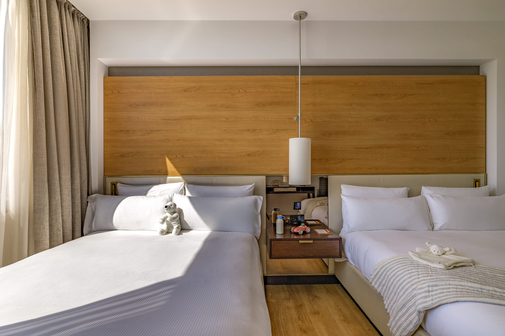 Modern hotel room with two beds, wood headboard, and kids' toys.