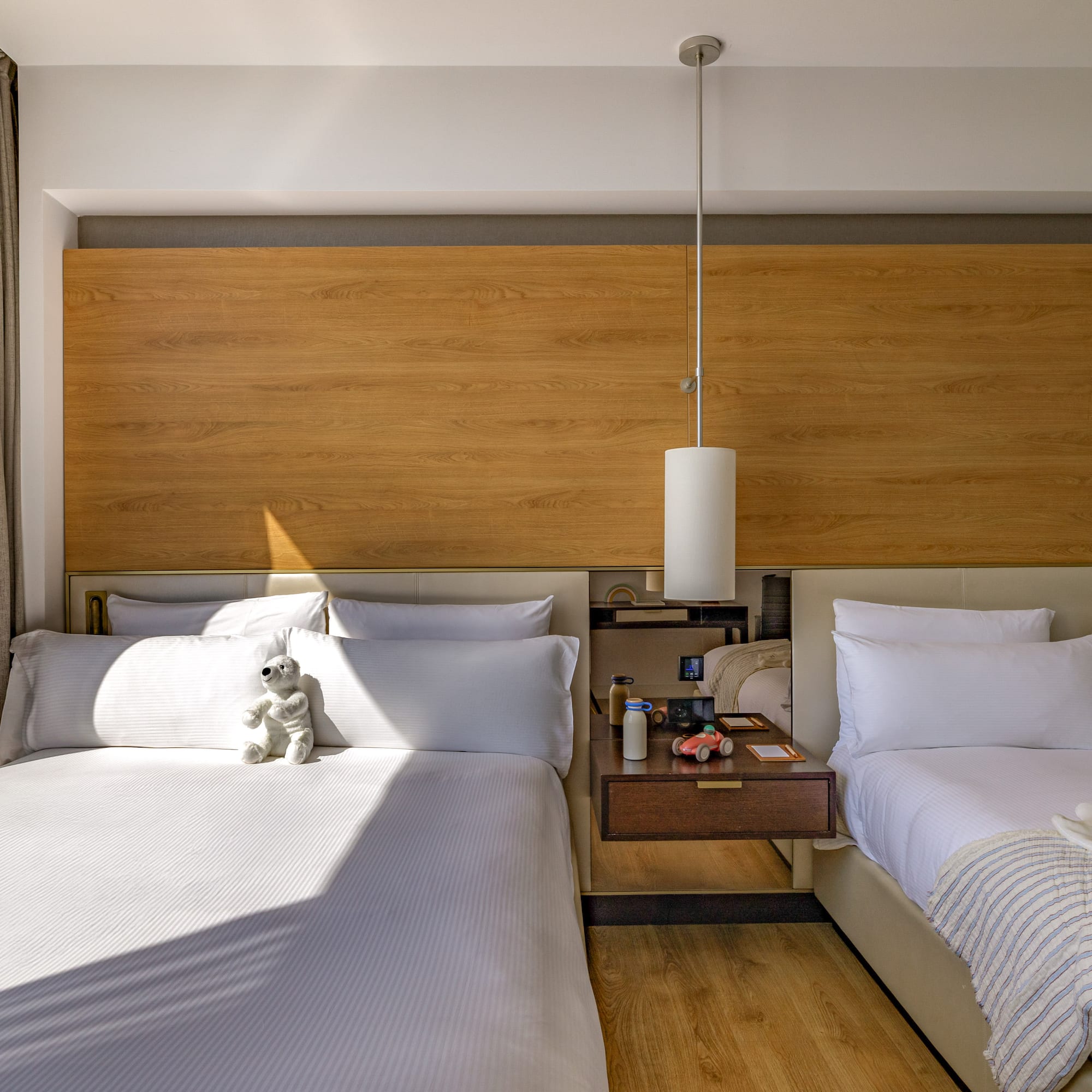 Modern hotel room with two beds, wood headboard, and kids' toys.