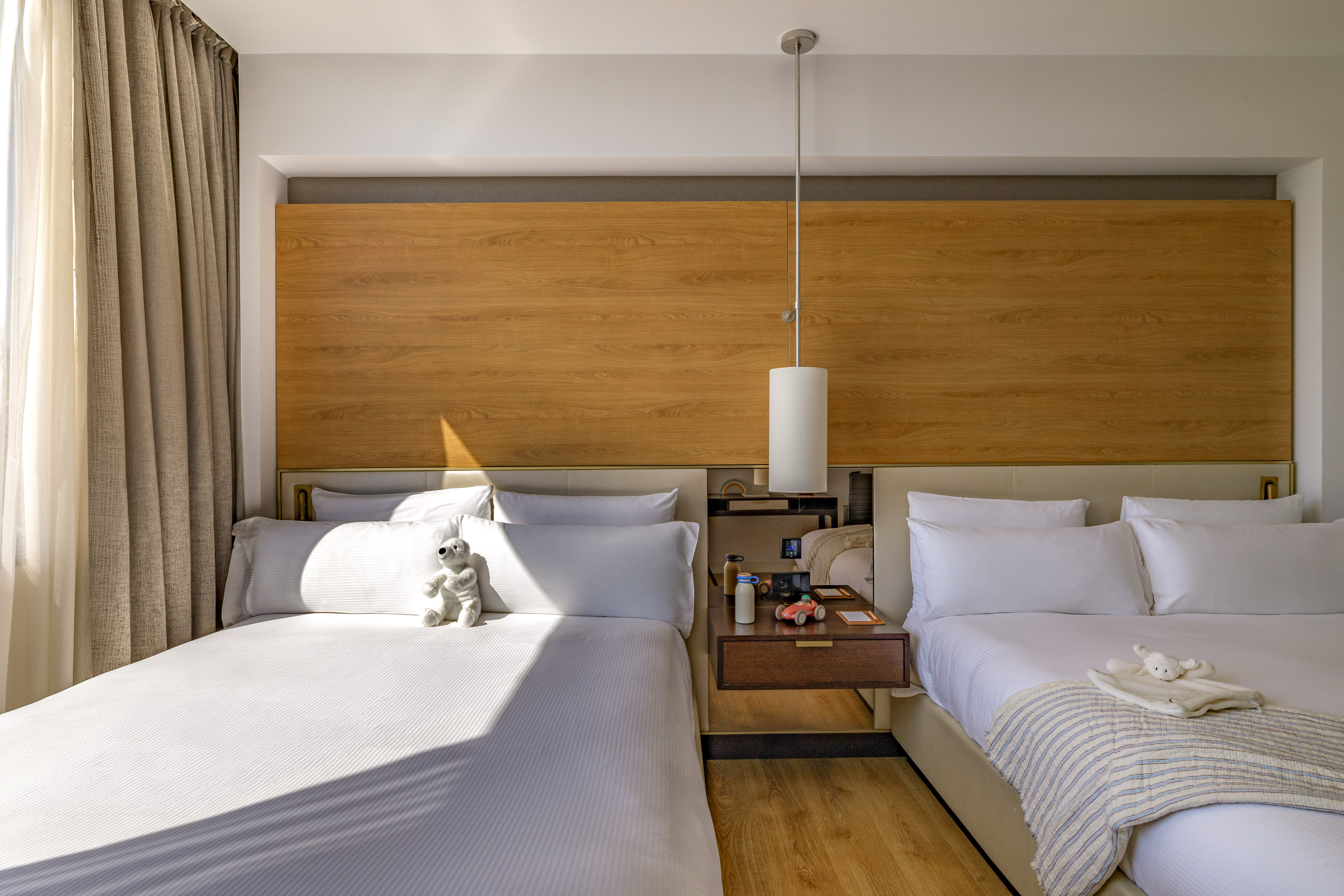 Modern hotel room with two beds, wood headboard, and kids' toys.