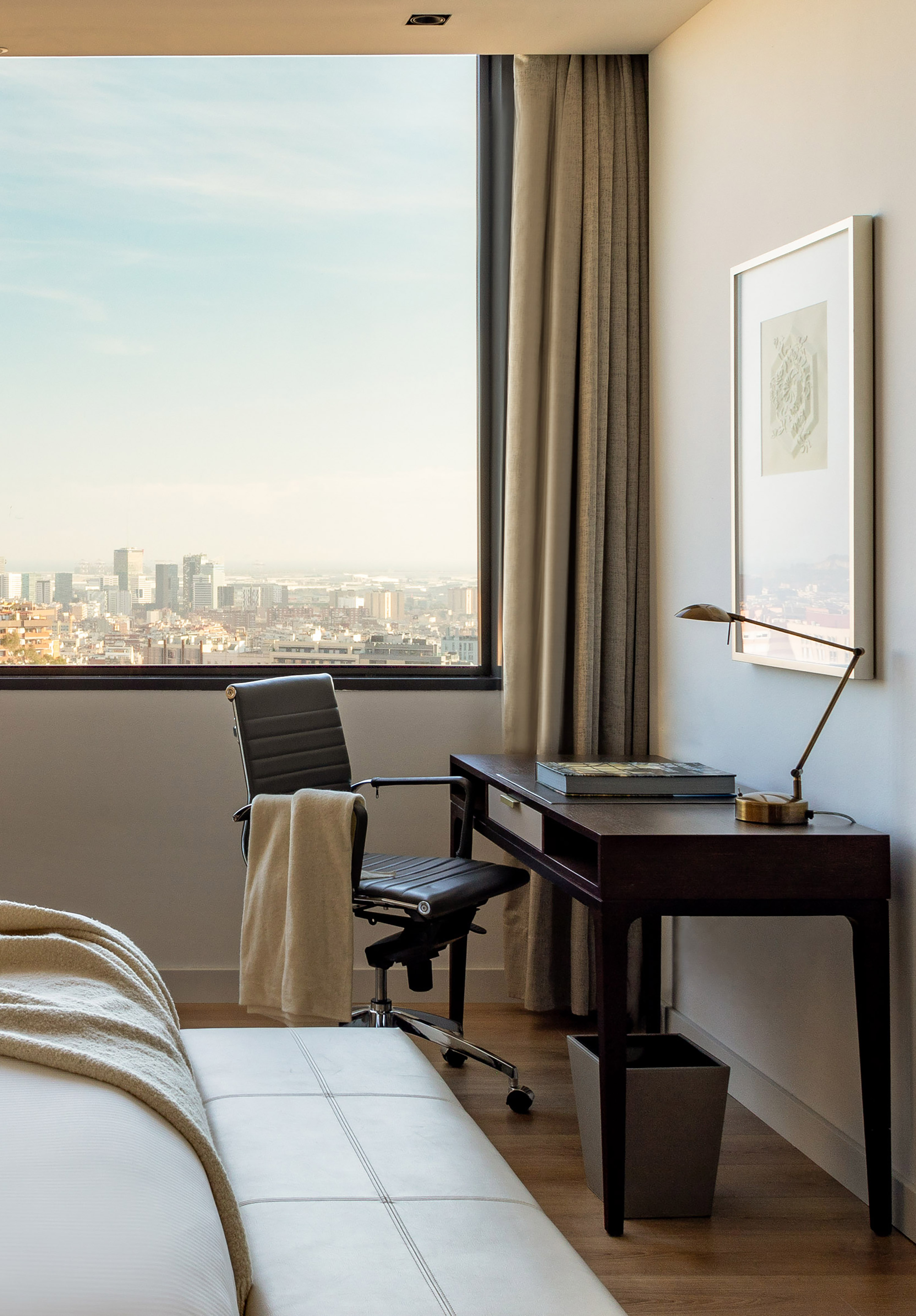 Modern hotel room desk with leather chair, city view, and reading lamp.
