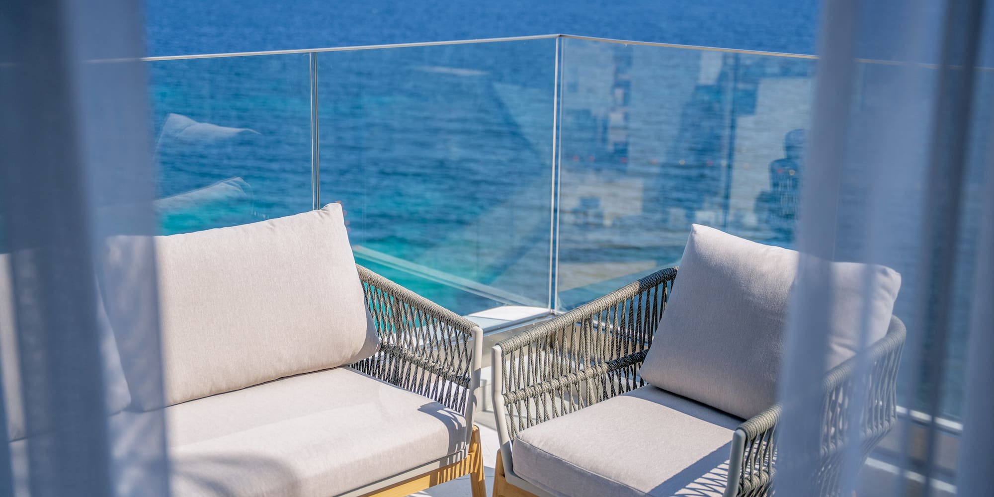 Modern balcony chairs overlooking a bright blue ocean with a distant boat.