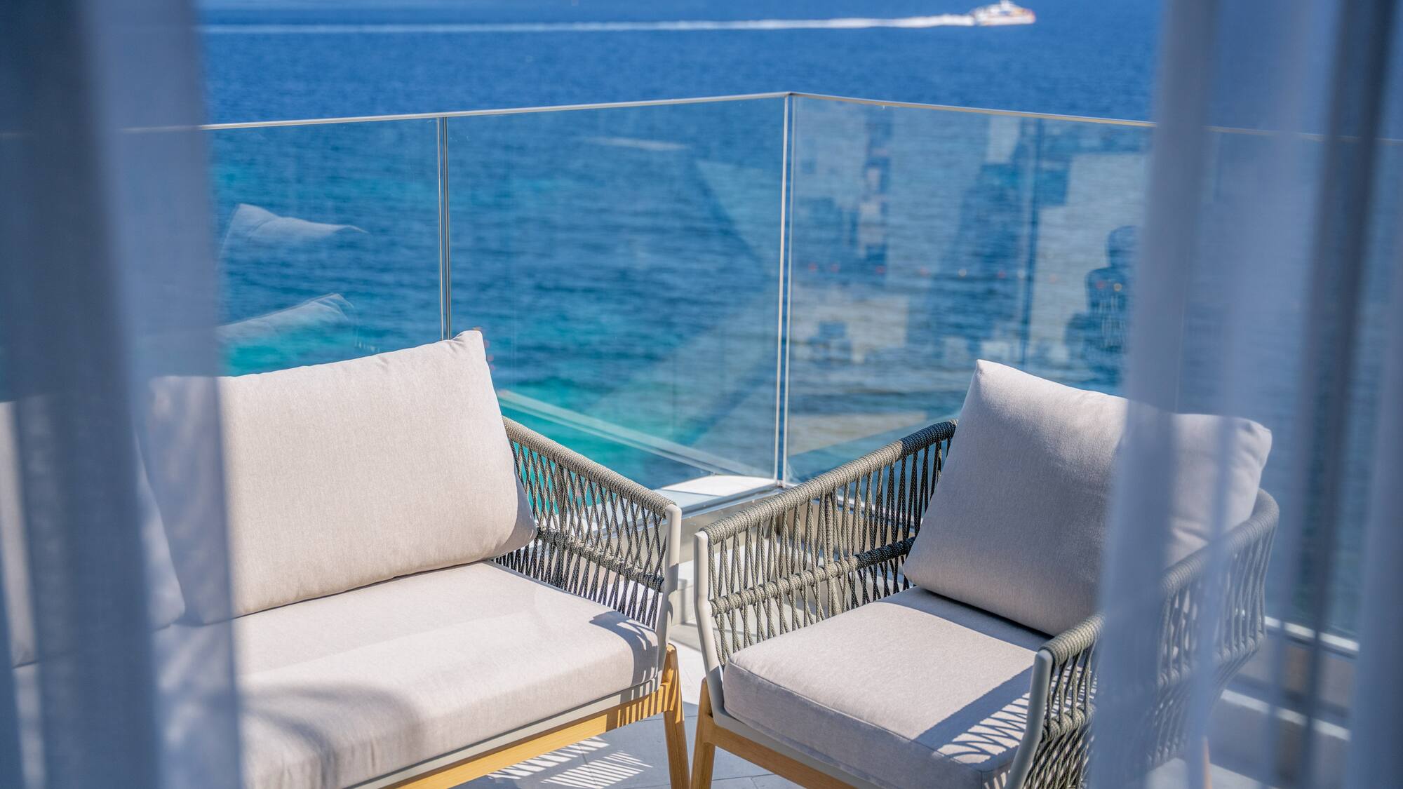 Modern balcony chairs overlooking a bright blue ocean with a distant boat.
