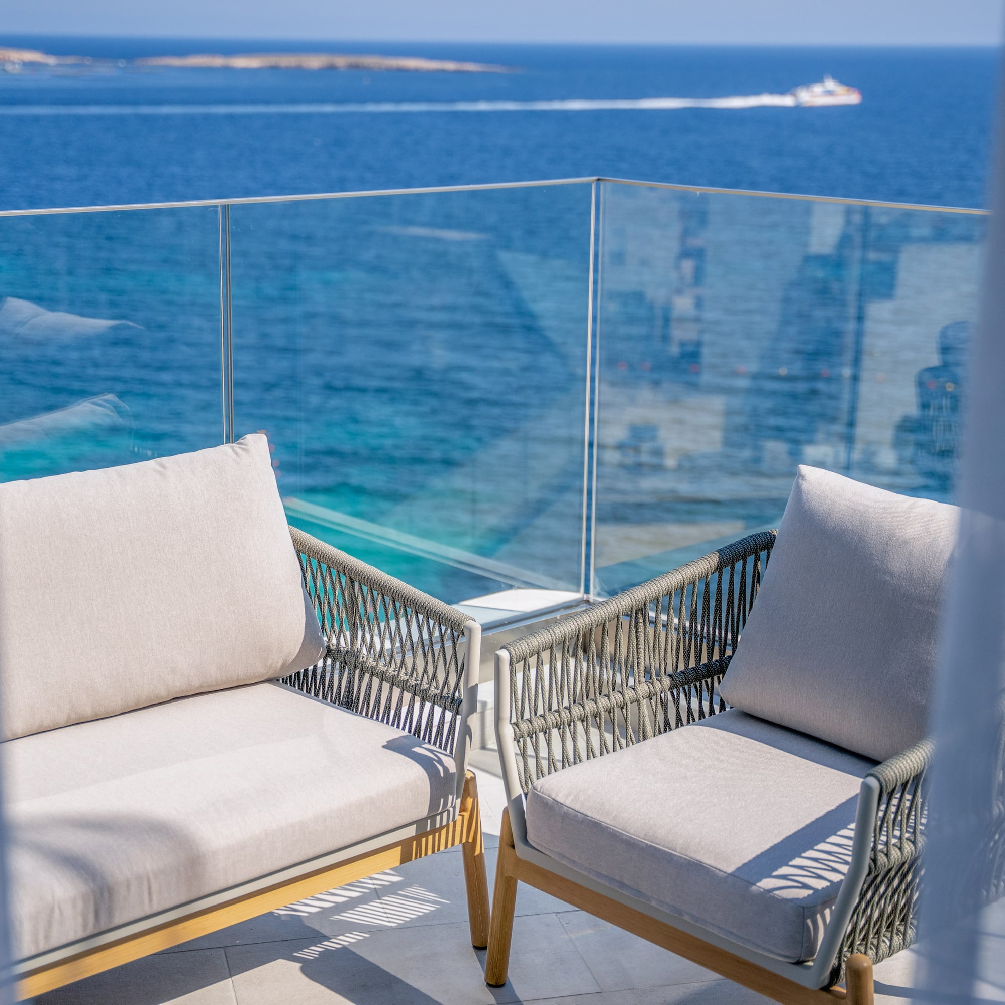 Modern balcony chairs overlooking a bright blue ocean with a distant boat.