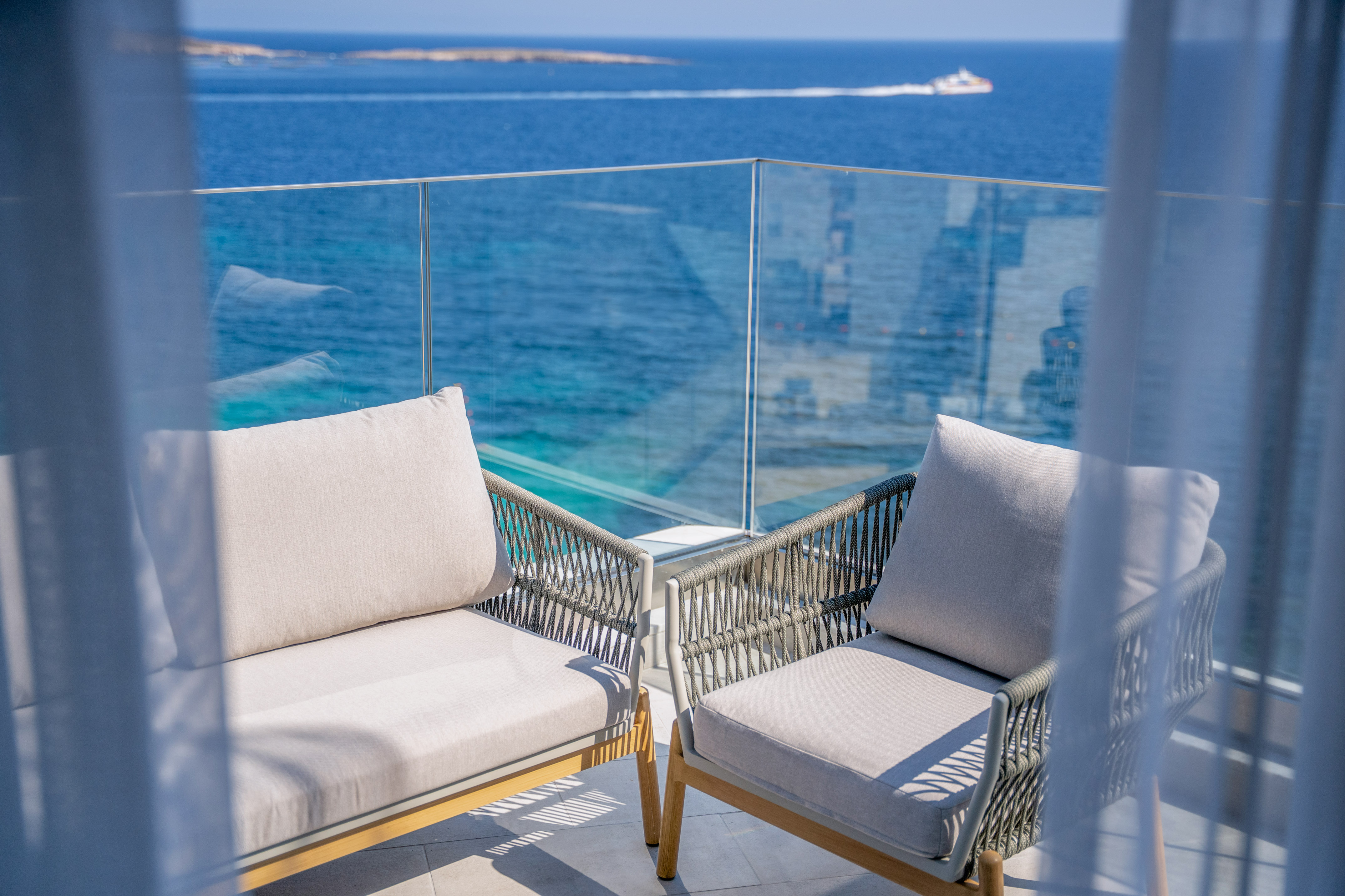 Modern balcony chairs overlooking a bright blue ocean with a distant boat.