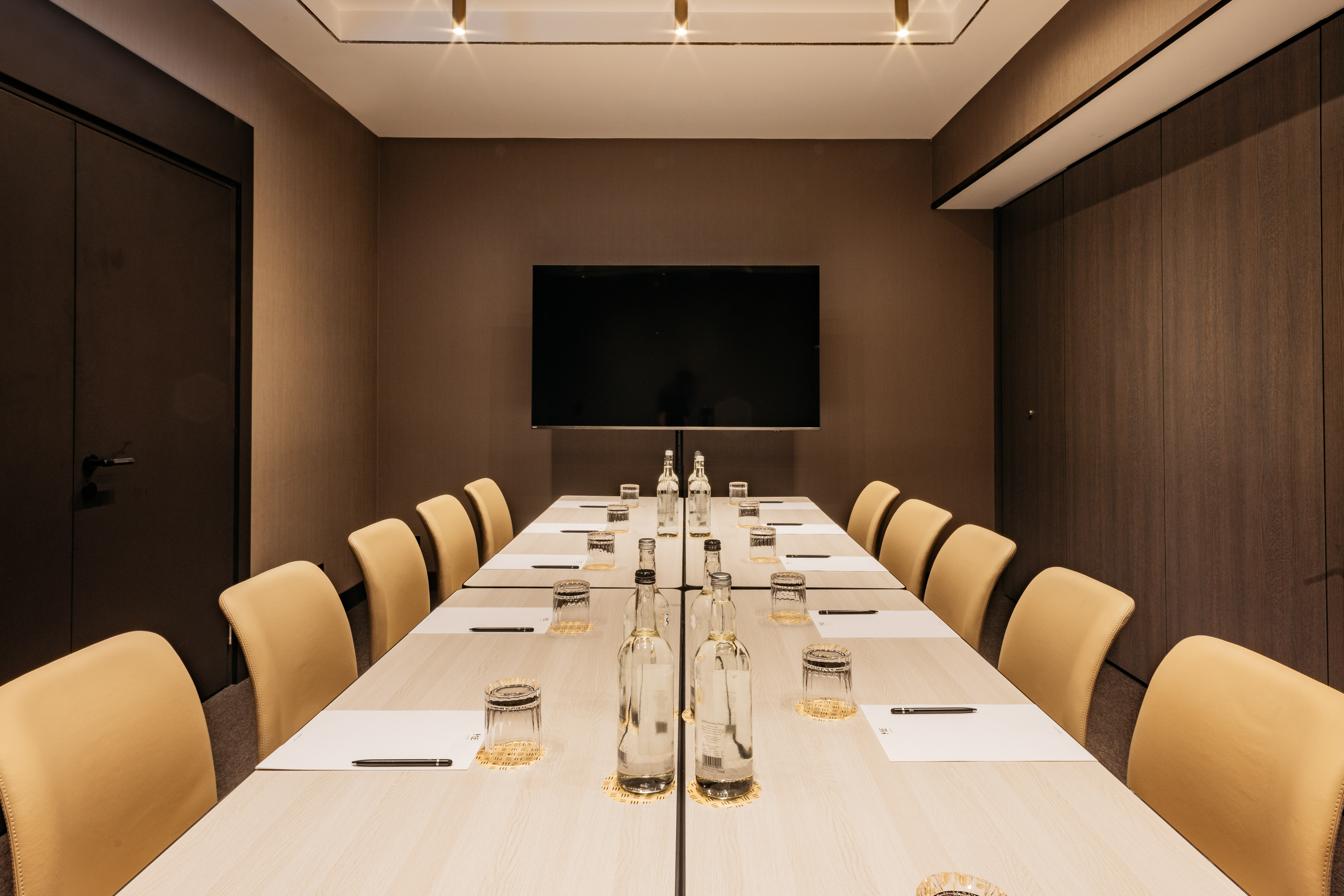 Modern meeting room with long table, beige chairs, and large TV screen.