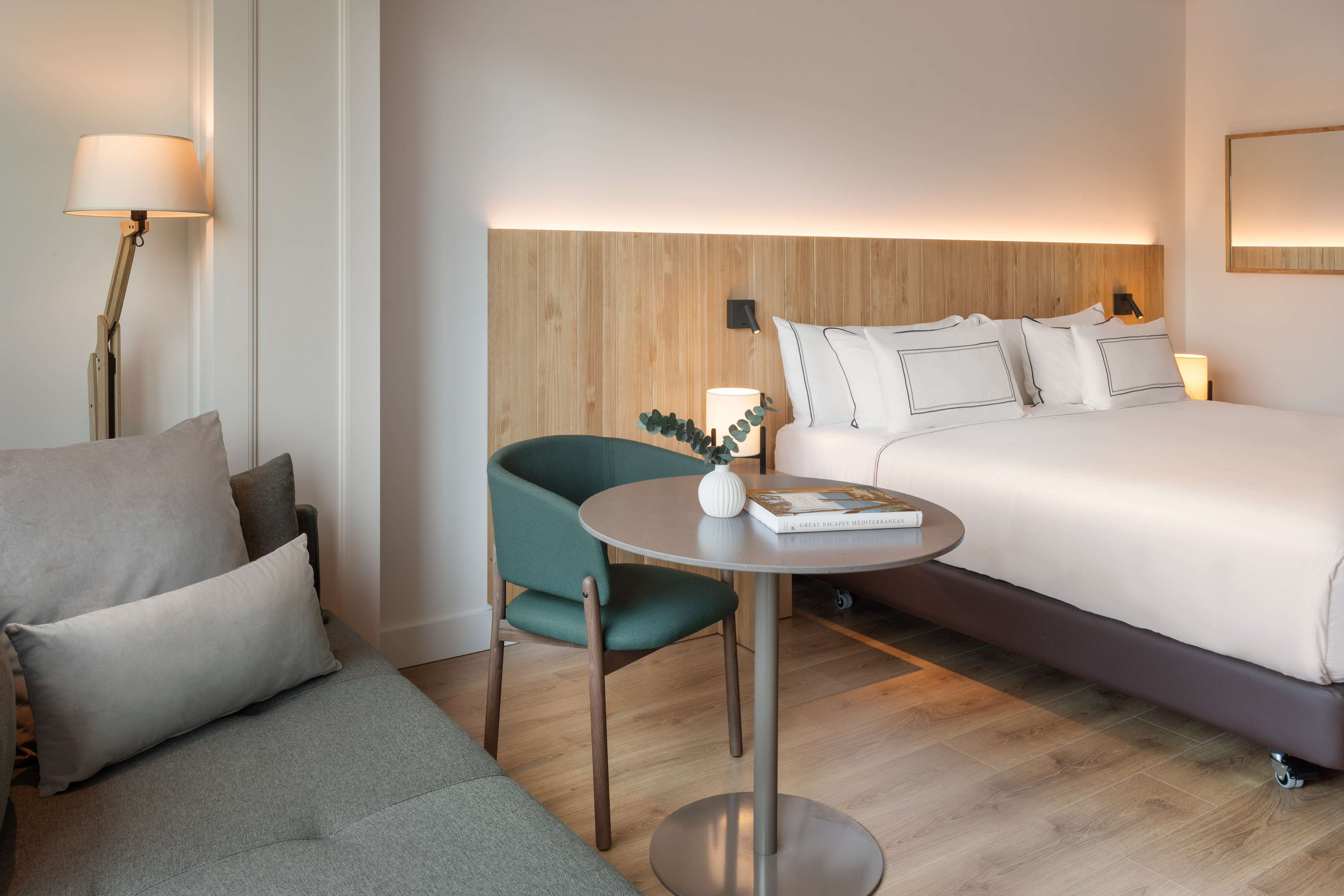 Modern hotel room with large bed, wooden headboard, sofa, and round table.
