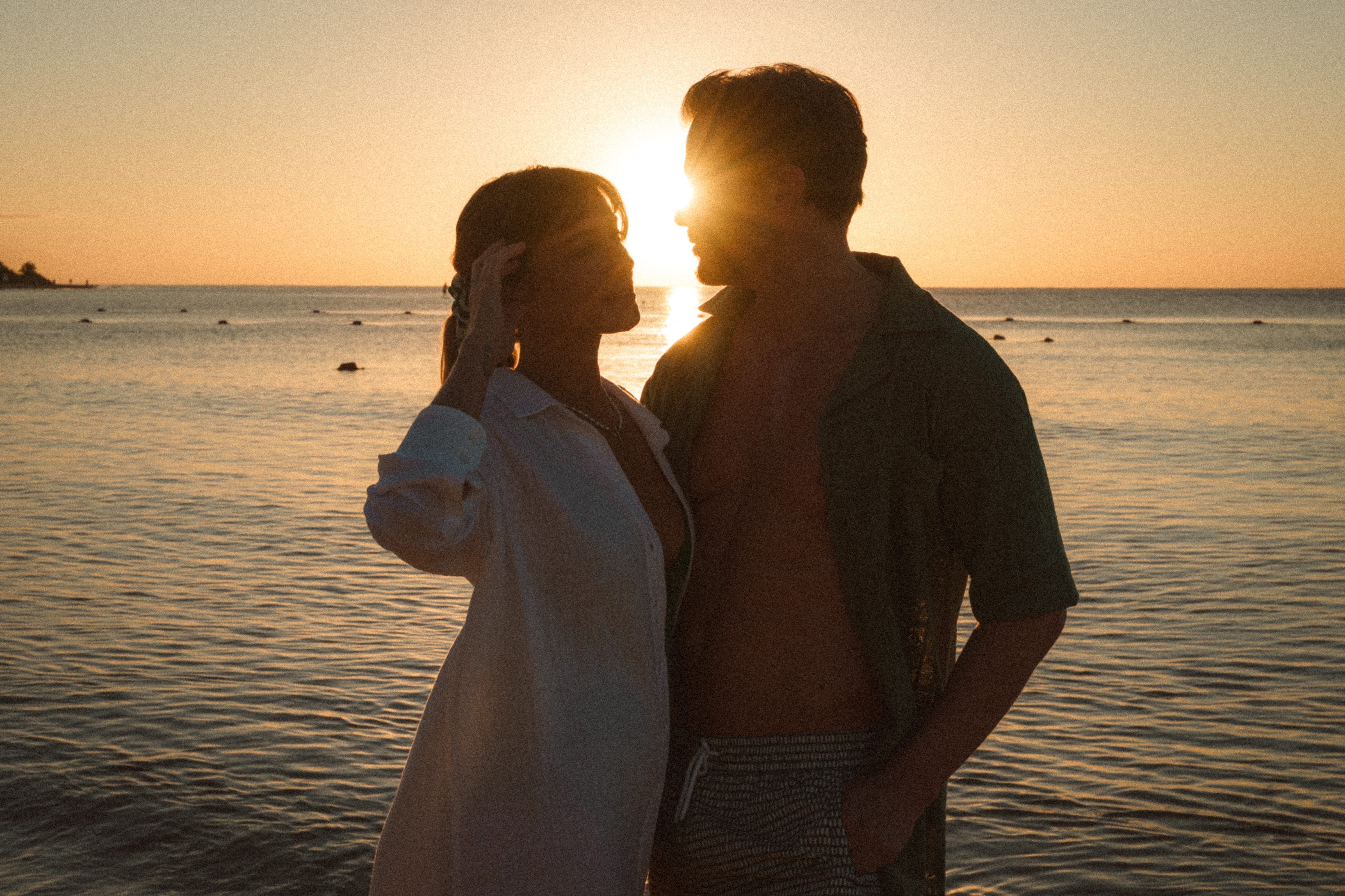 Romantic couple silhouette at sunset by the ocean, golden light.