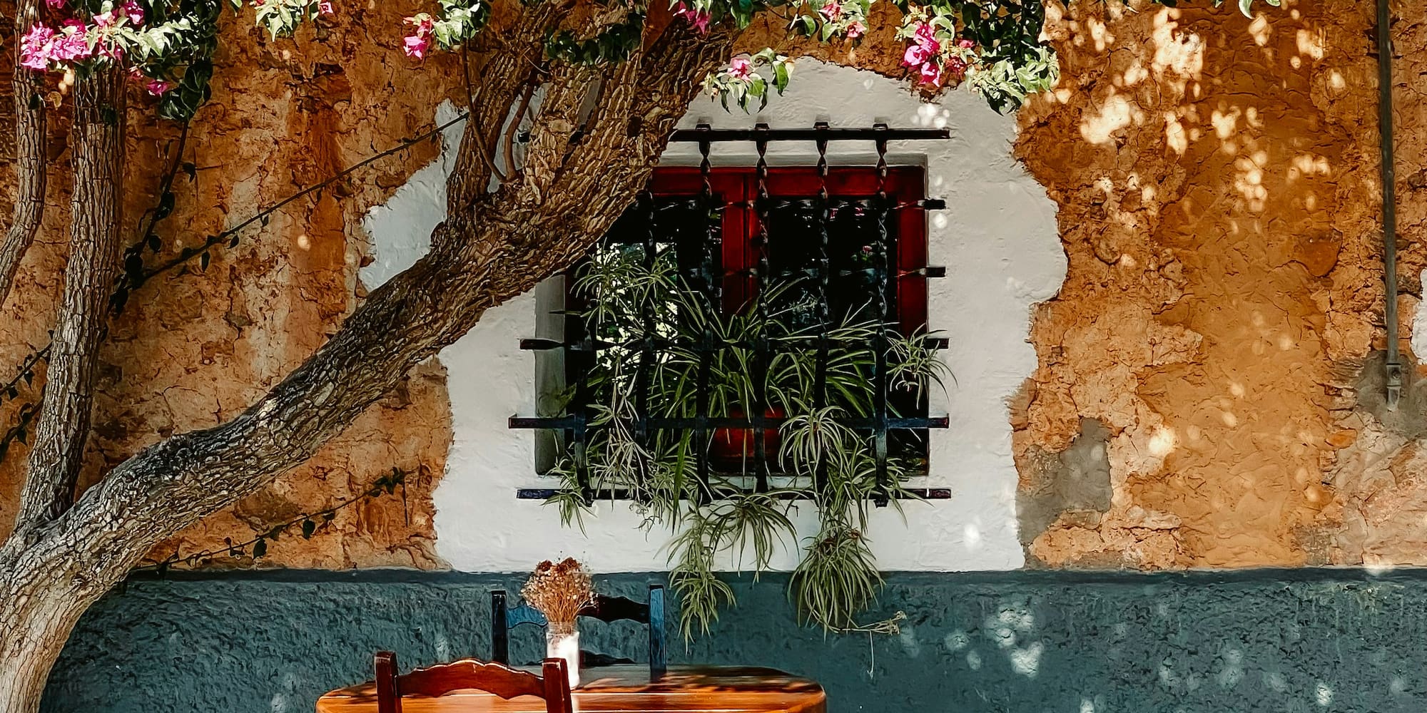 Rustic patio with wooden table, chairs, and vibrant pink bougainvillea.