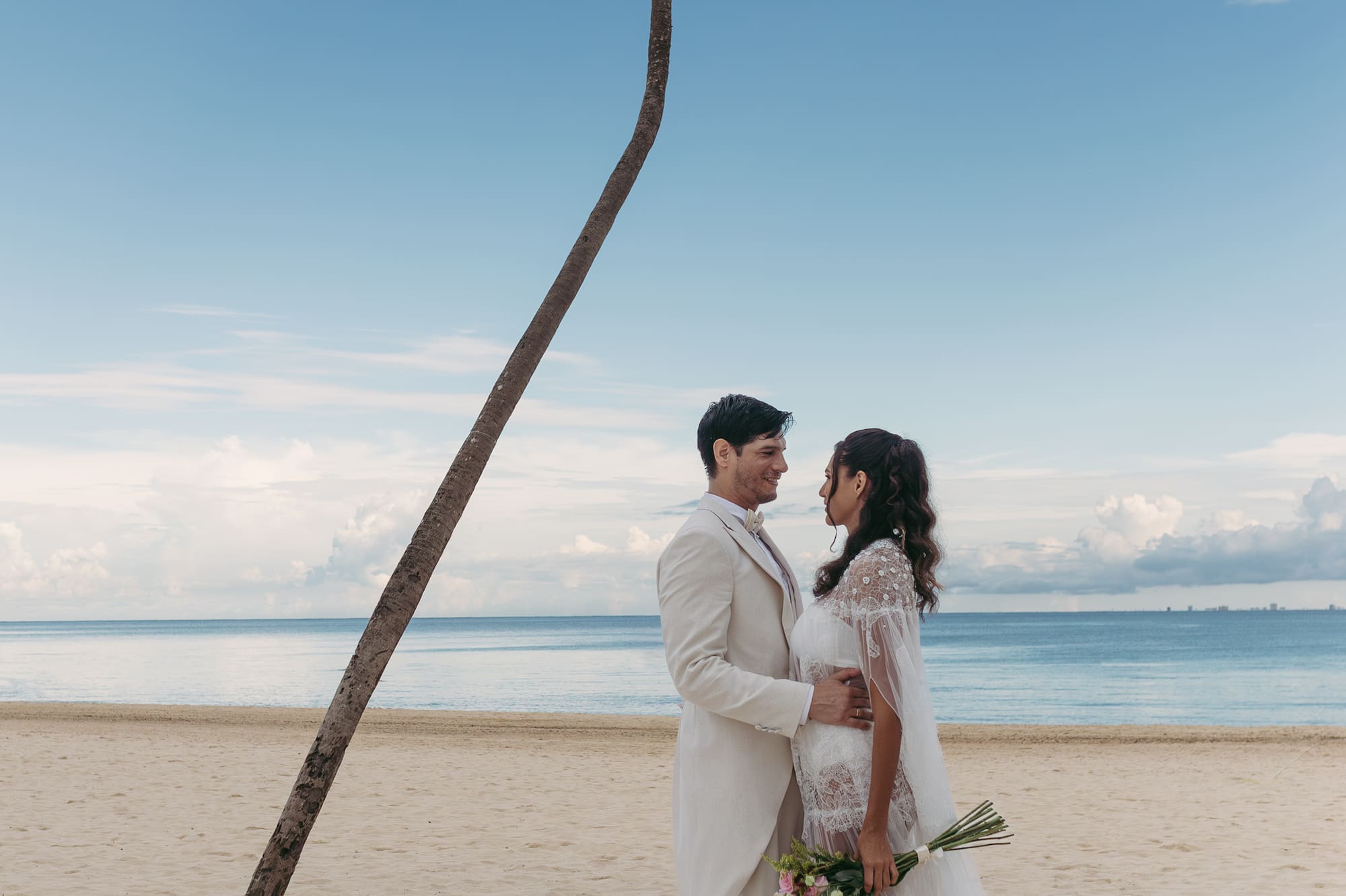 a man and woman in white suit on a beach with a palm tree