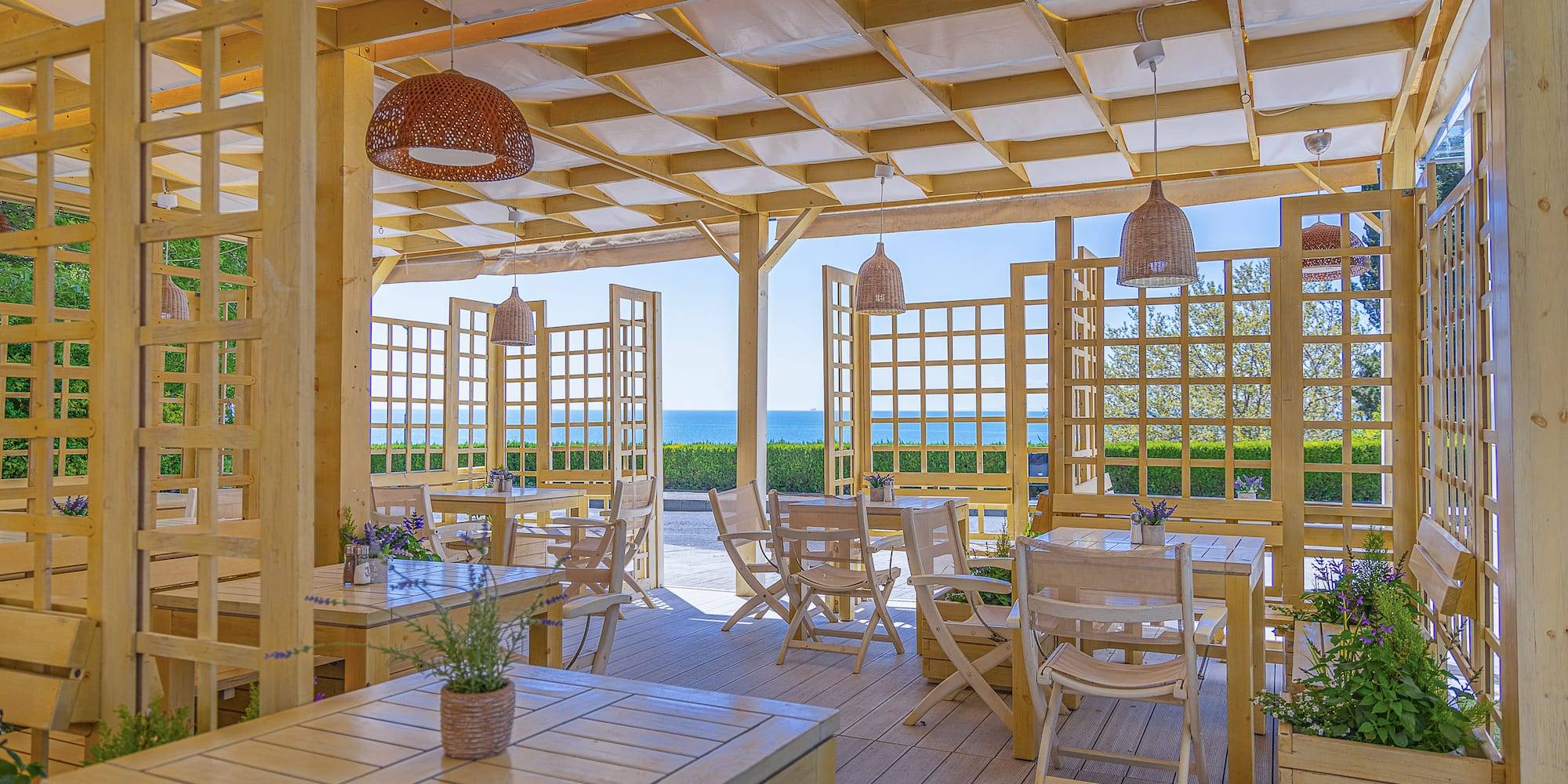 Outdoor restaurant terrace with wooden pergola, tables, and sea view.