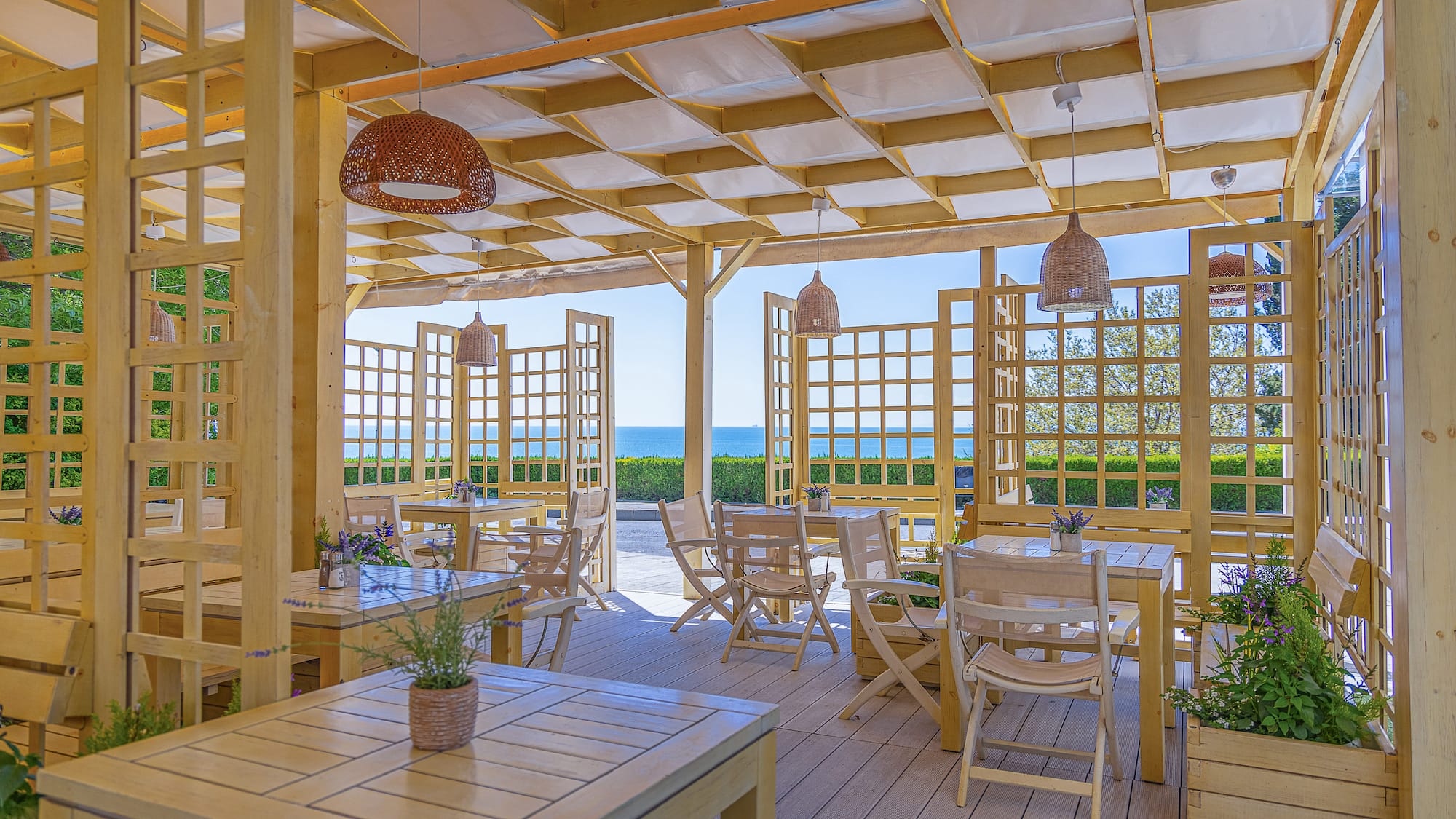 Outdoor restaurant terrace with wooden pergola, tables, and sea view.
