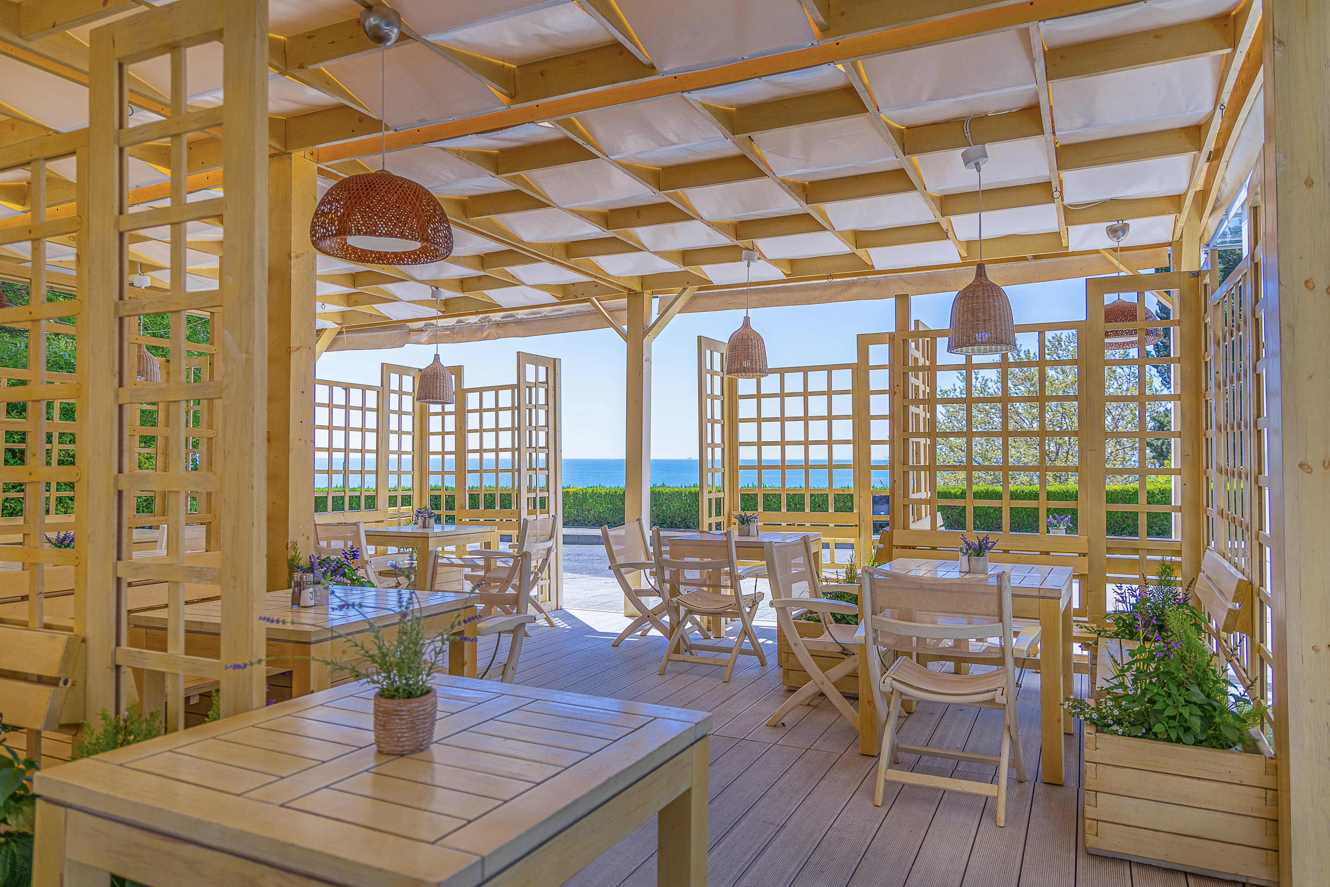 Outdoor restaurant terrace with wooden pergola, tables, and sea view.