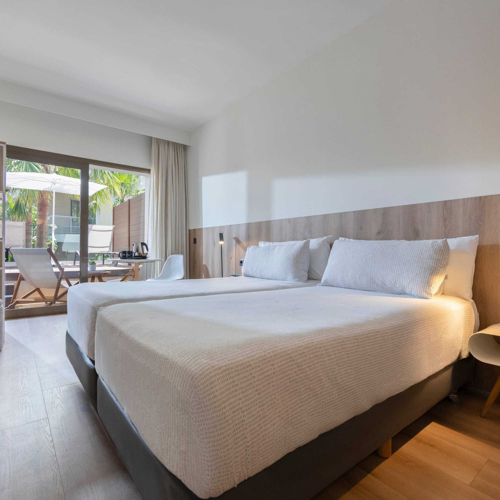 Bright hotel room with twin beds, wooden floor, and outdoor patio.