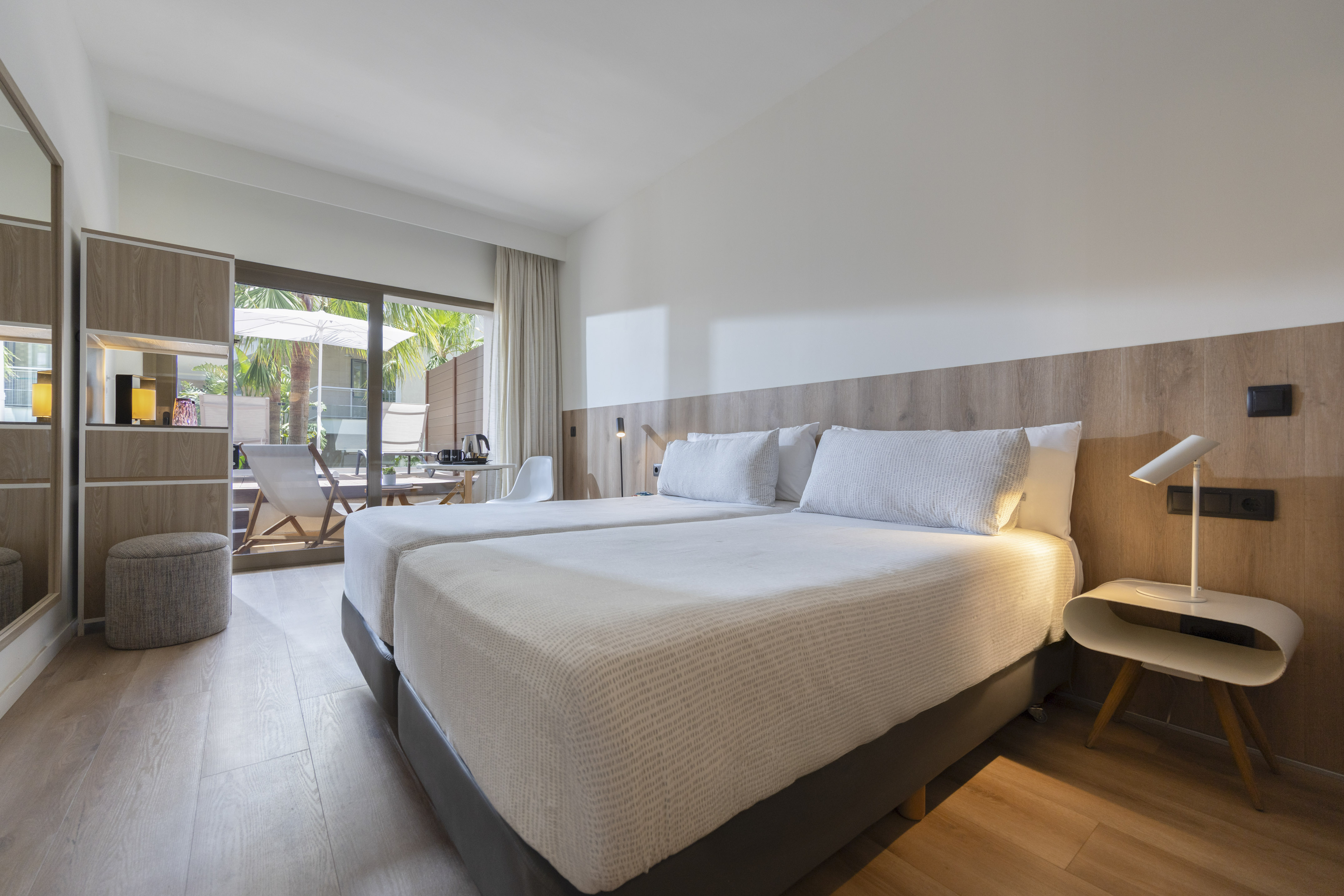 Bright hotel room with twin beds, wooden floor, and outdoor patio.