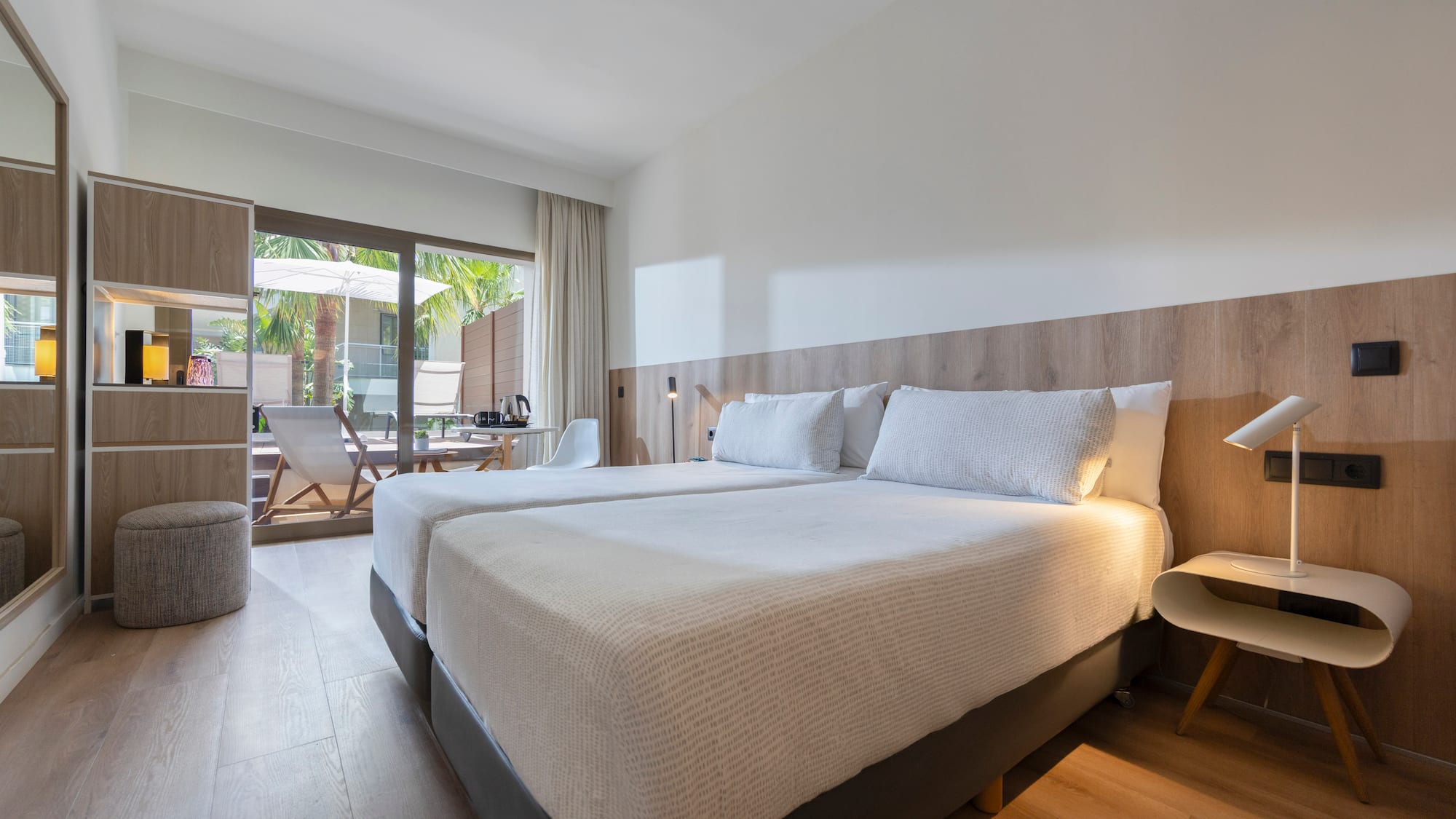 Bright hotel room with twin beds, wooden floor, and outdoor patio.