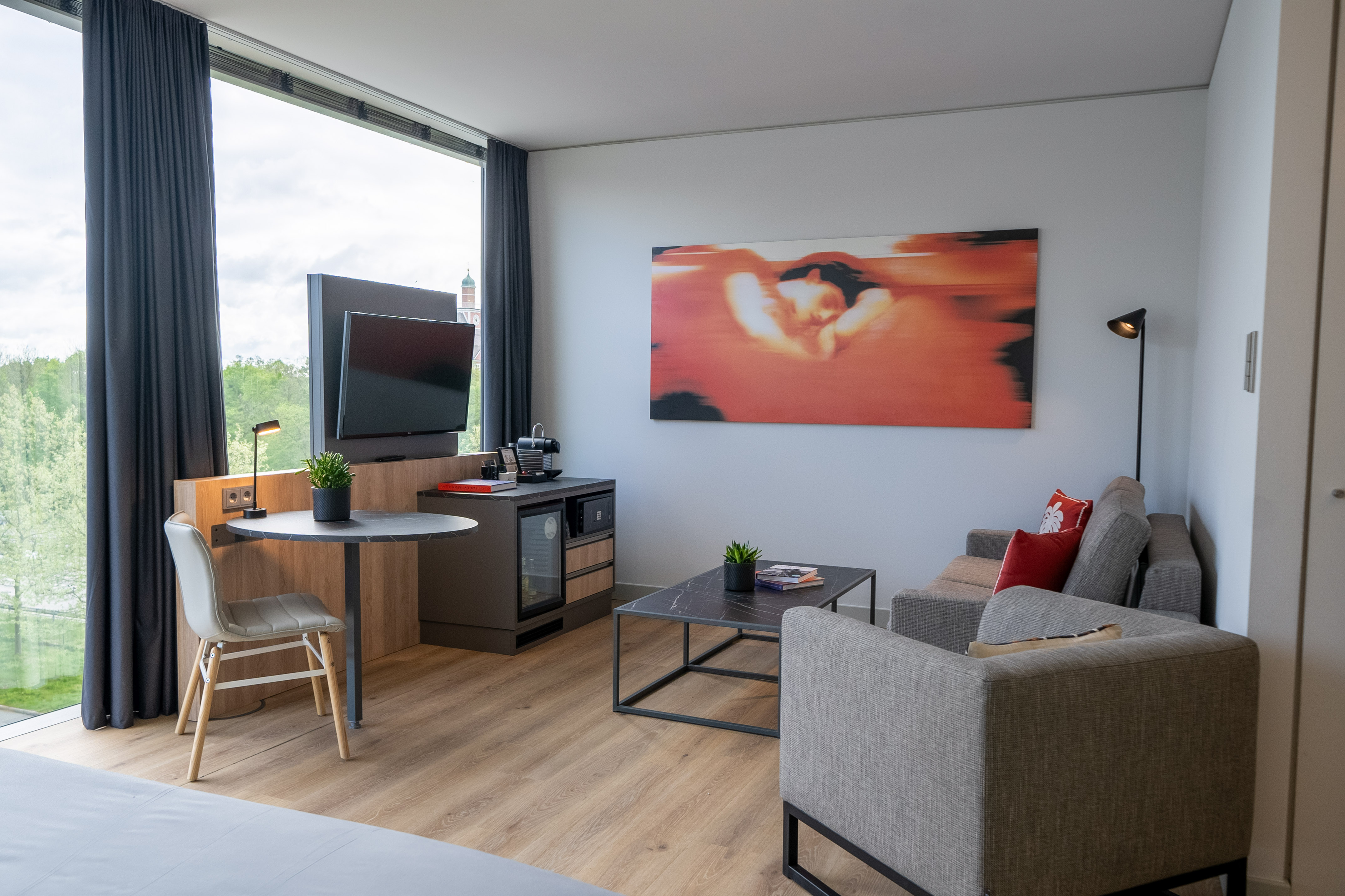 Modern hotel suite interior with living area, desk, large window, abstract art.