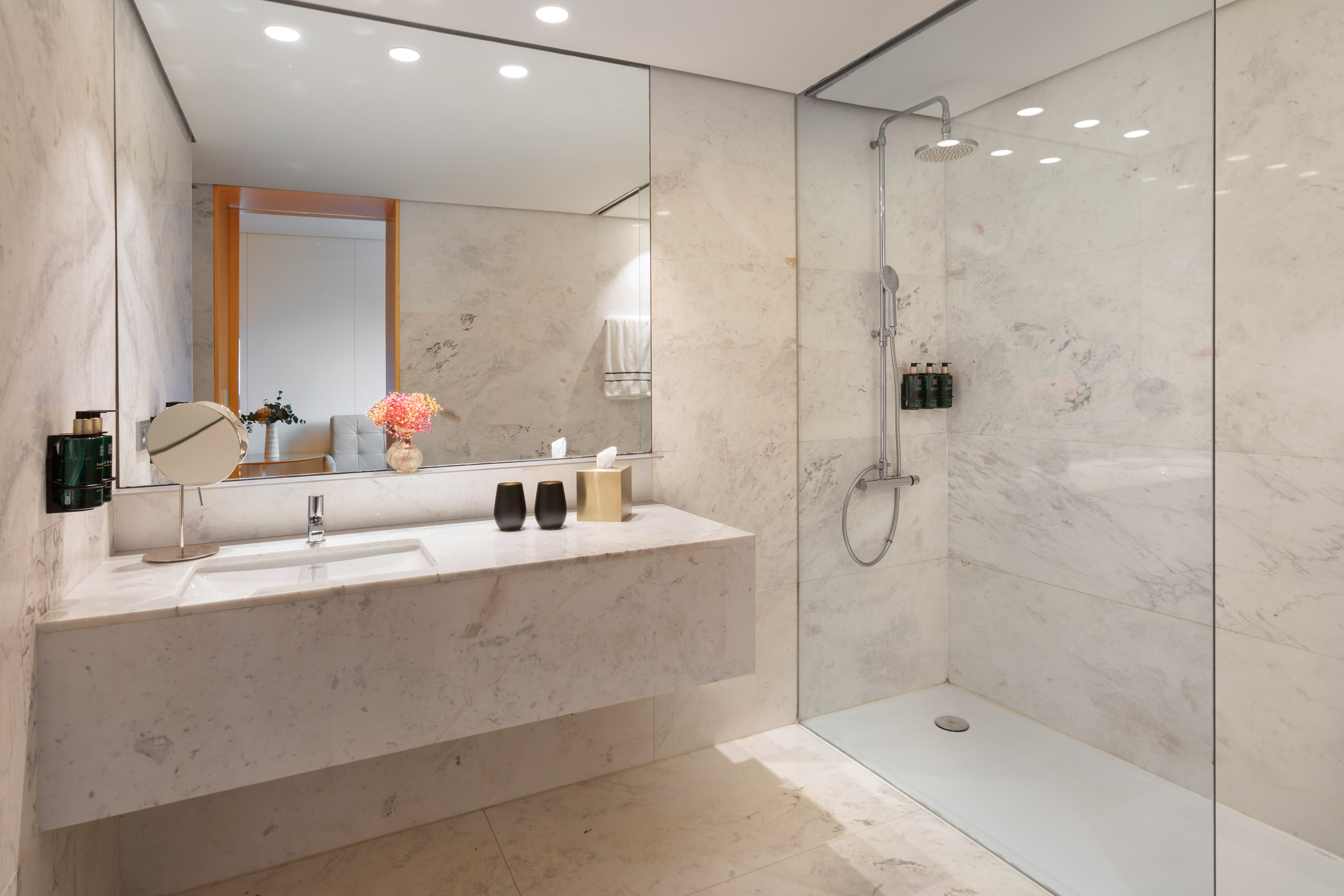 Modern luxury hotel bathroom with marble vanity and glass shower.