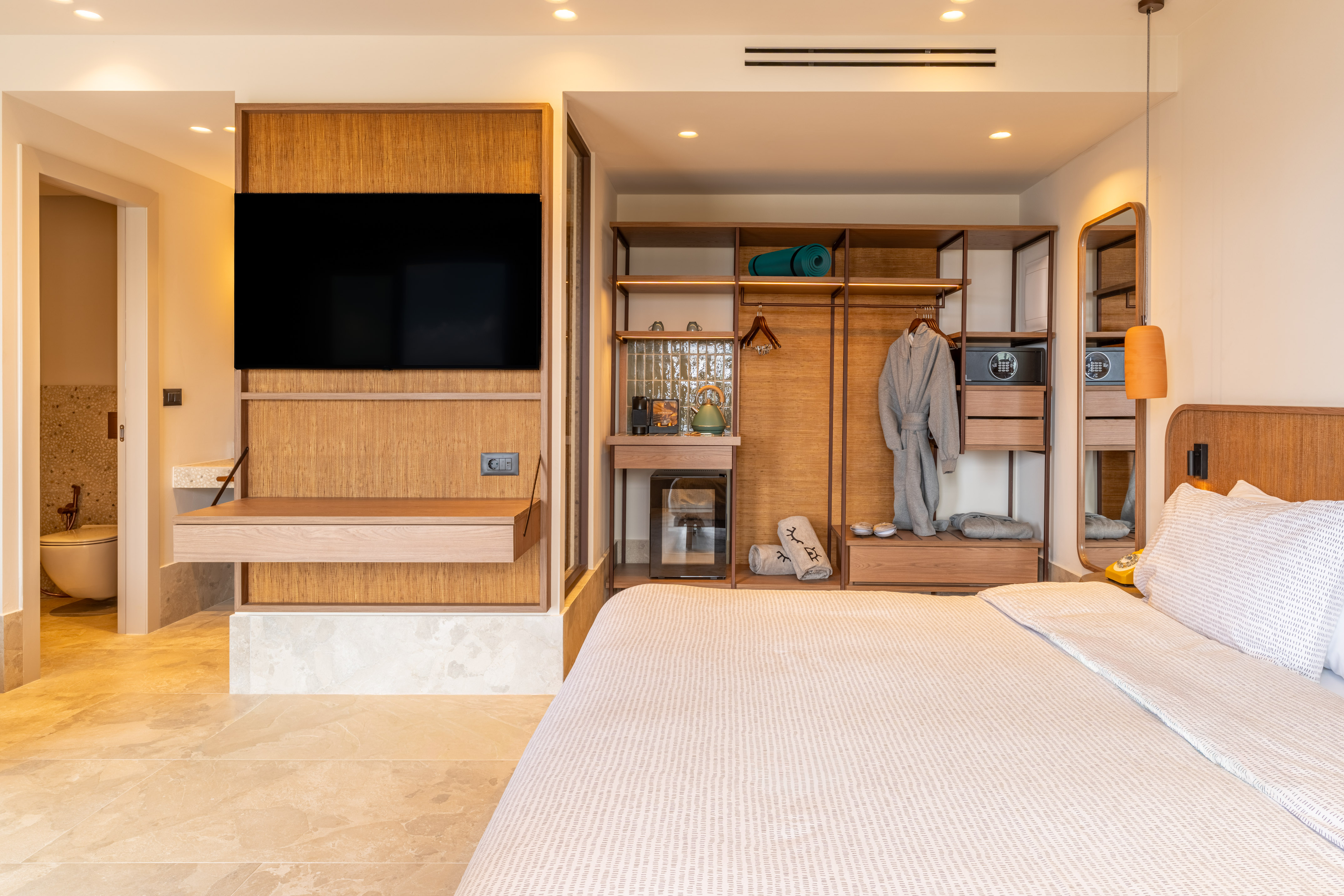 Modern hotel room with wooden TV wall, built-in wardrobe, and comfortable bed.