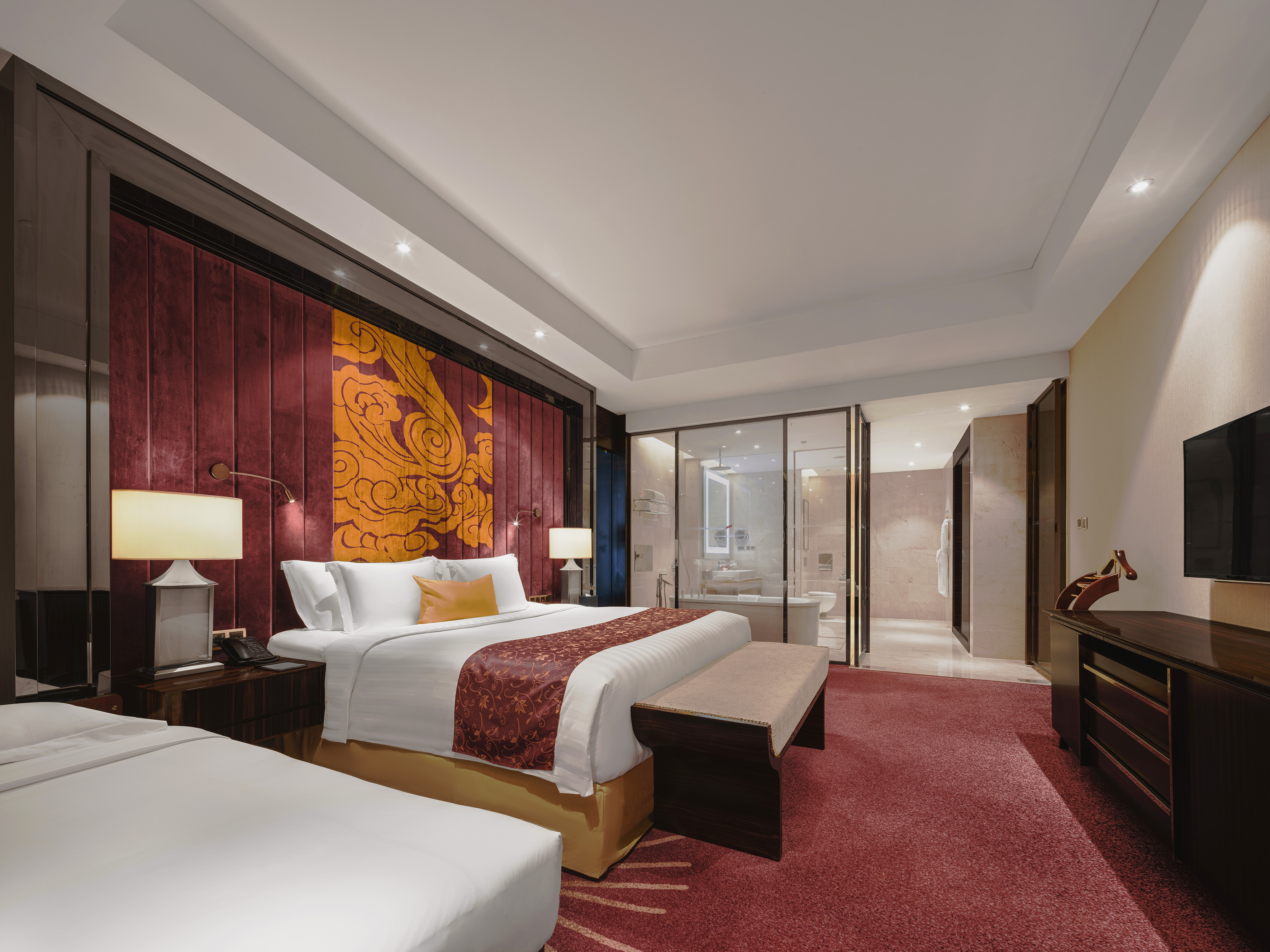 Luxury hotel bedroom with ornate red headboard and glass ensuite bathroom.