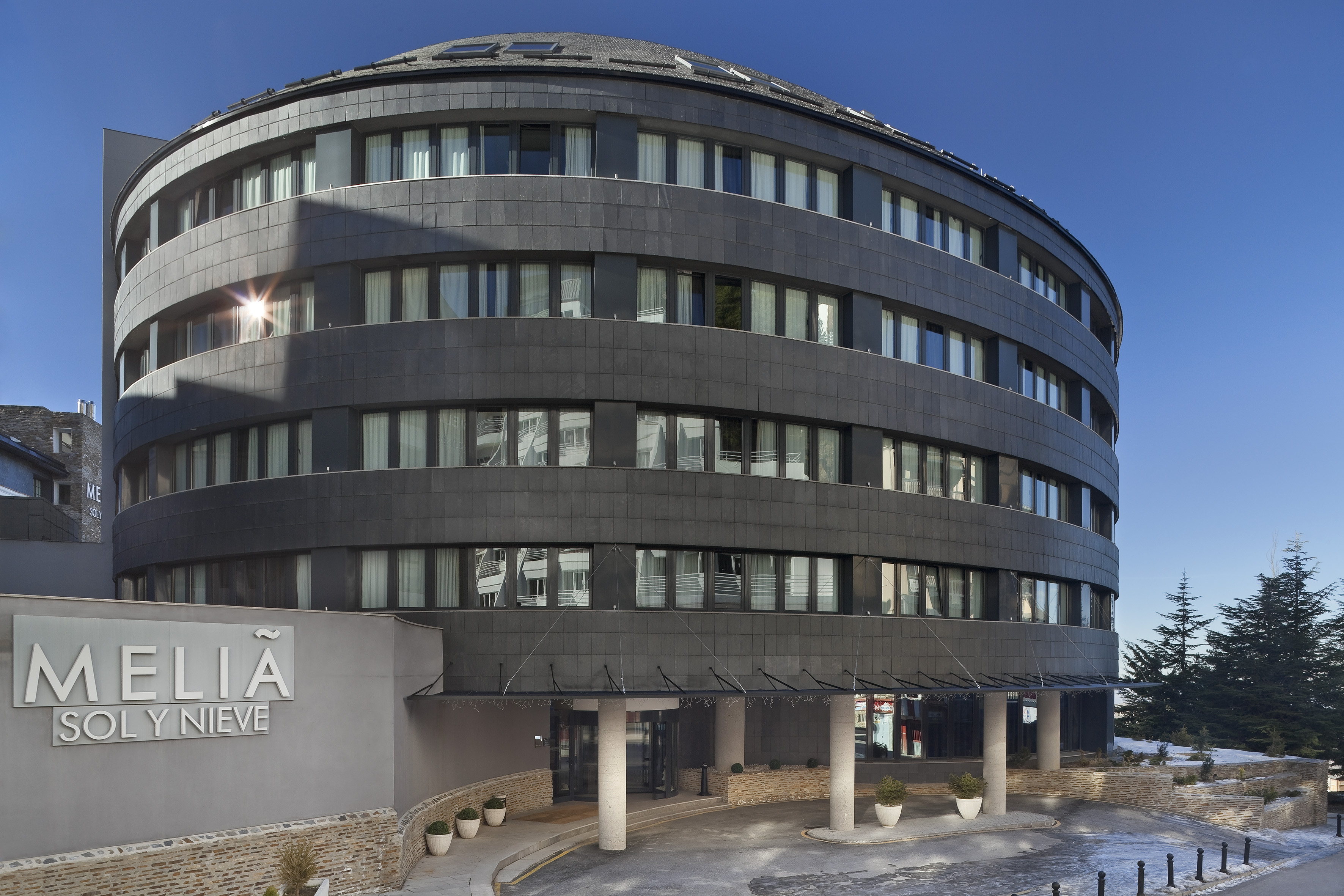Meliá Sol y Nieve hotel. Dark, curved building with snow and blue sky.