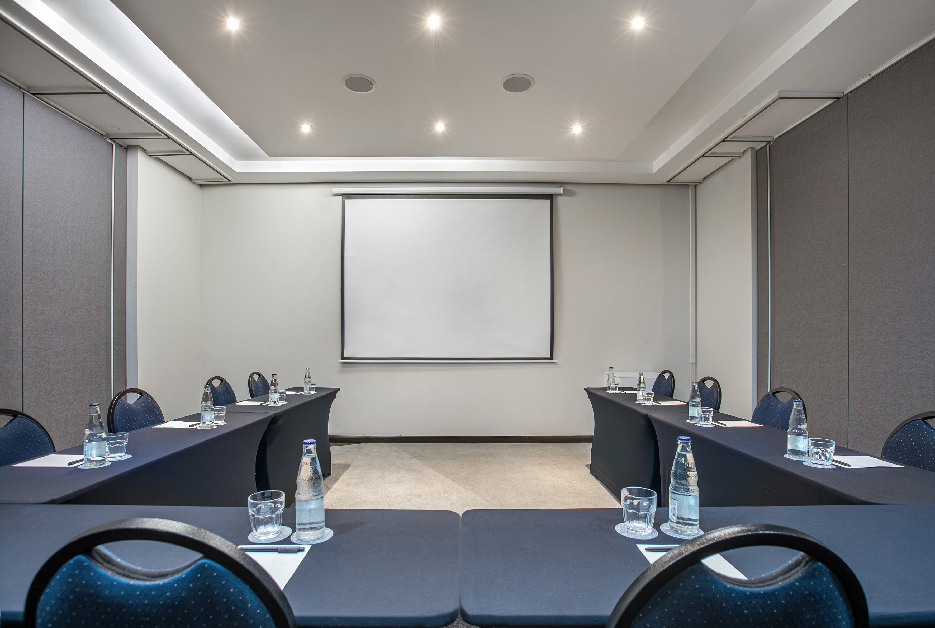Modern conference room setup with presentation screen, tables, and bottled water.