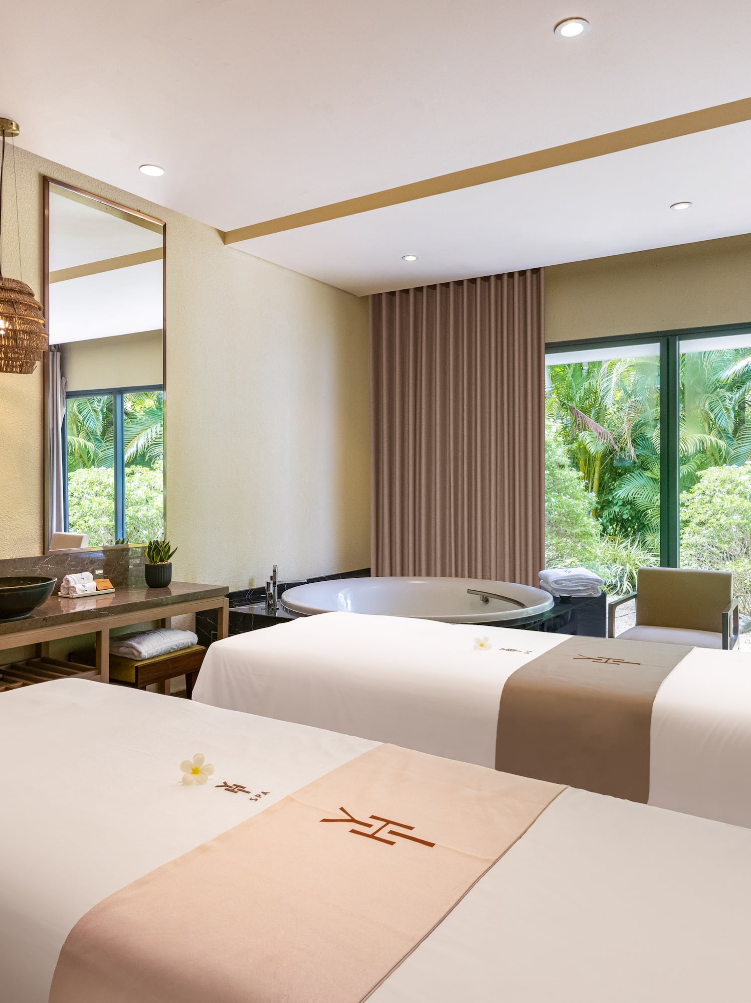 Luxury spa room with two massage tables, bathtub, and tropical garden view.