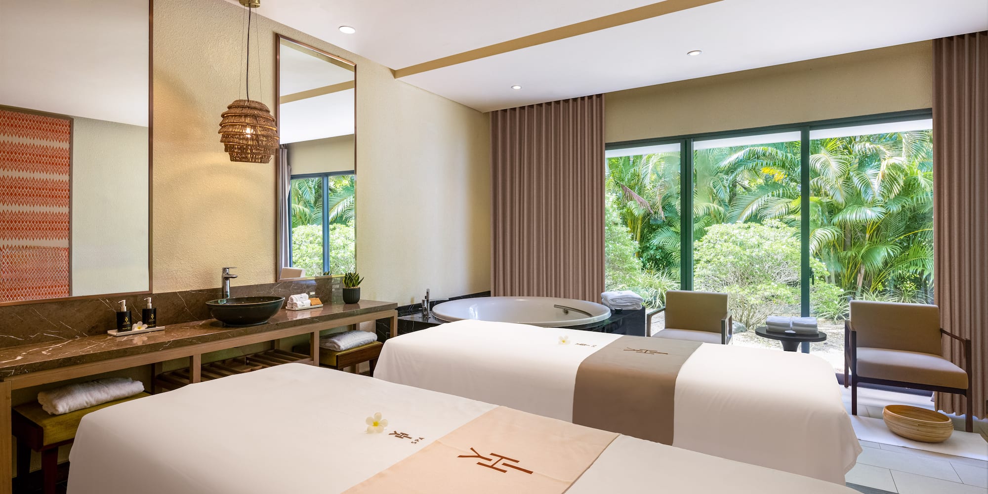 Serene spa treatment room with dual massage beds, soaking tub, and tropical view.