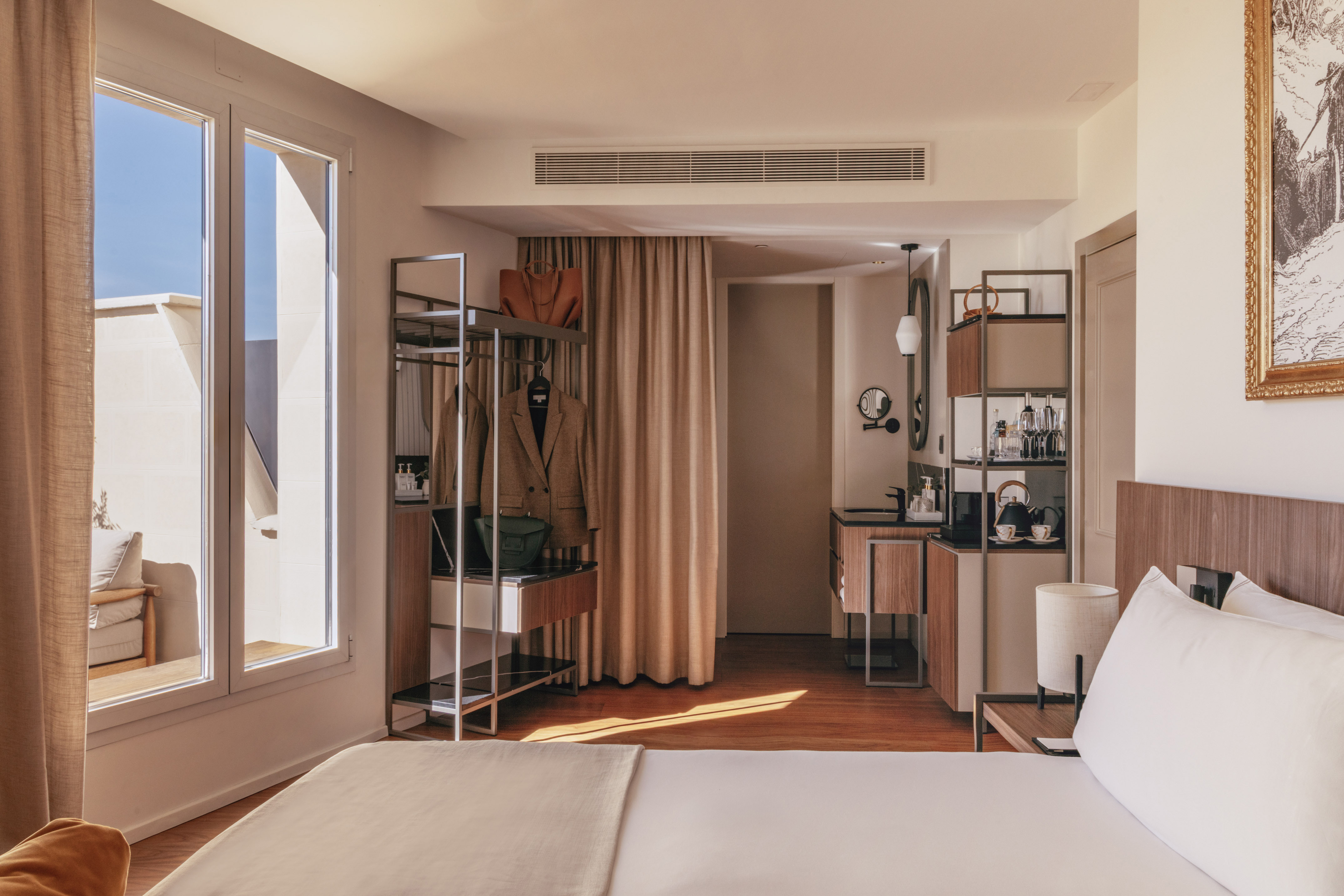 Bright modern hotel room with bed, balcony view, and open wardrobe.