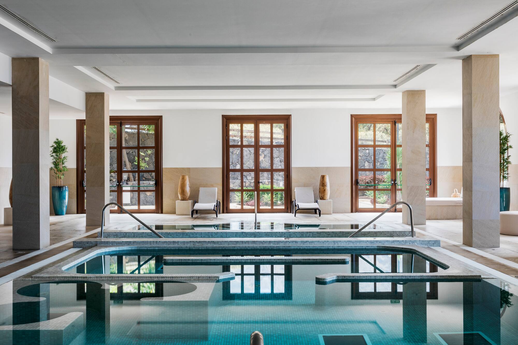 Indoor spa hydrotherapy pool with large windows and lounge chairs.