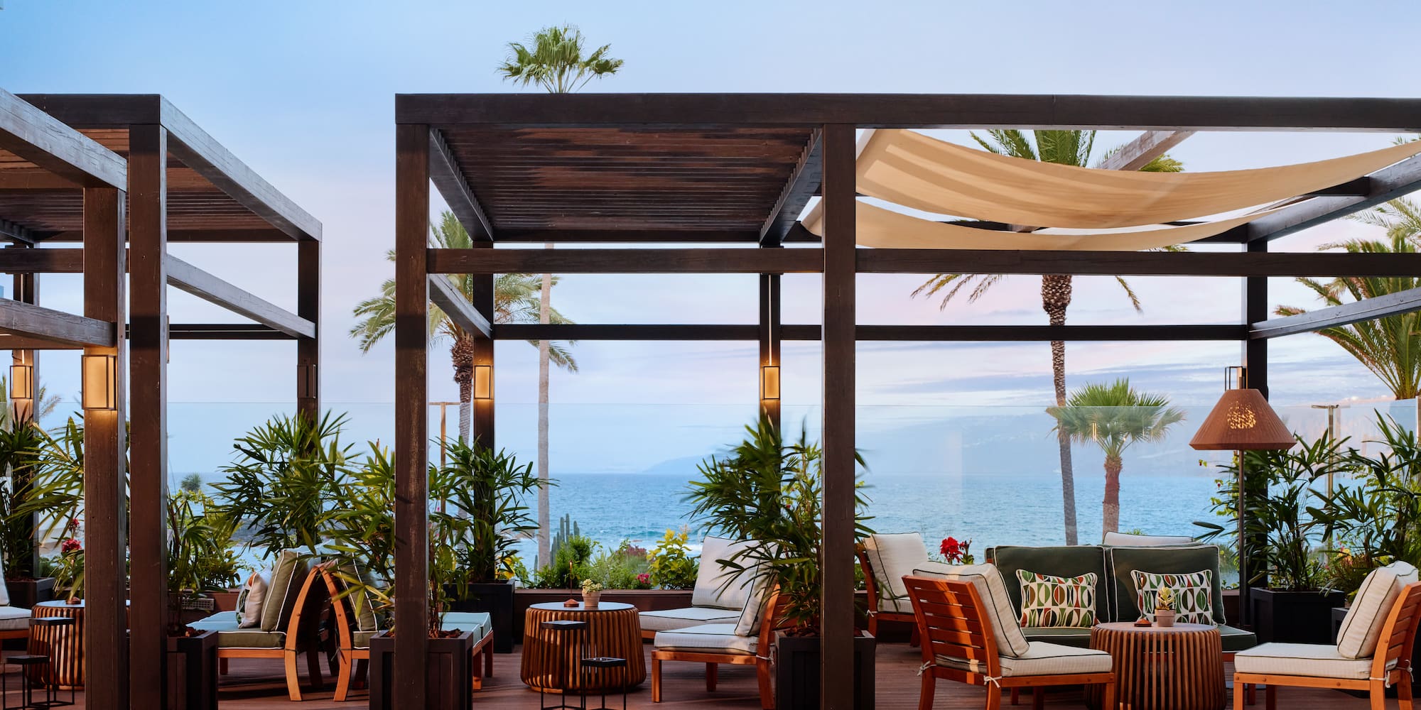 Luxury oceanfront lounge with pergolas, tropical plants, and sea view.
