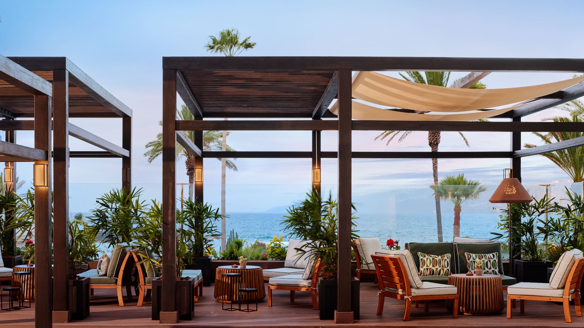 Ocean view outdoor lounge with wooden pergola, resort patio furniture, and palm trees.