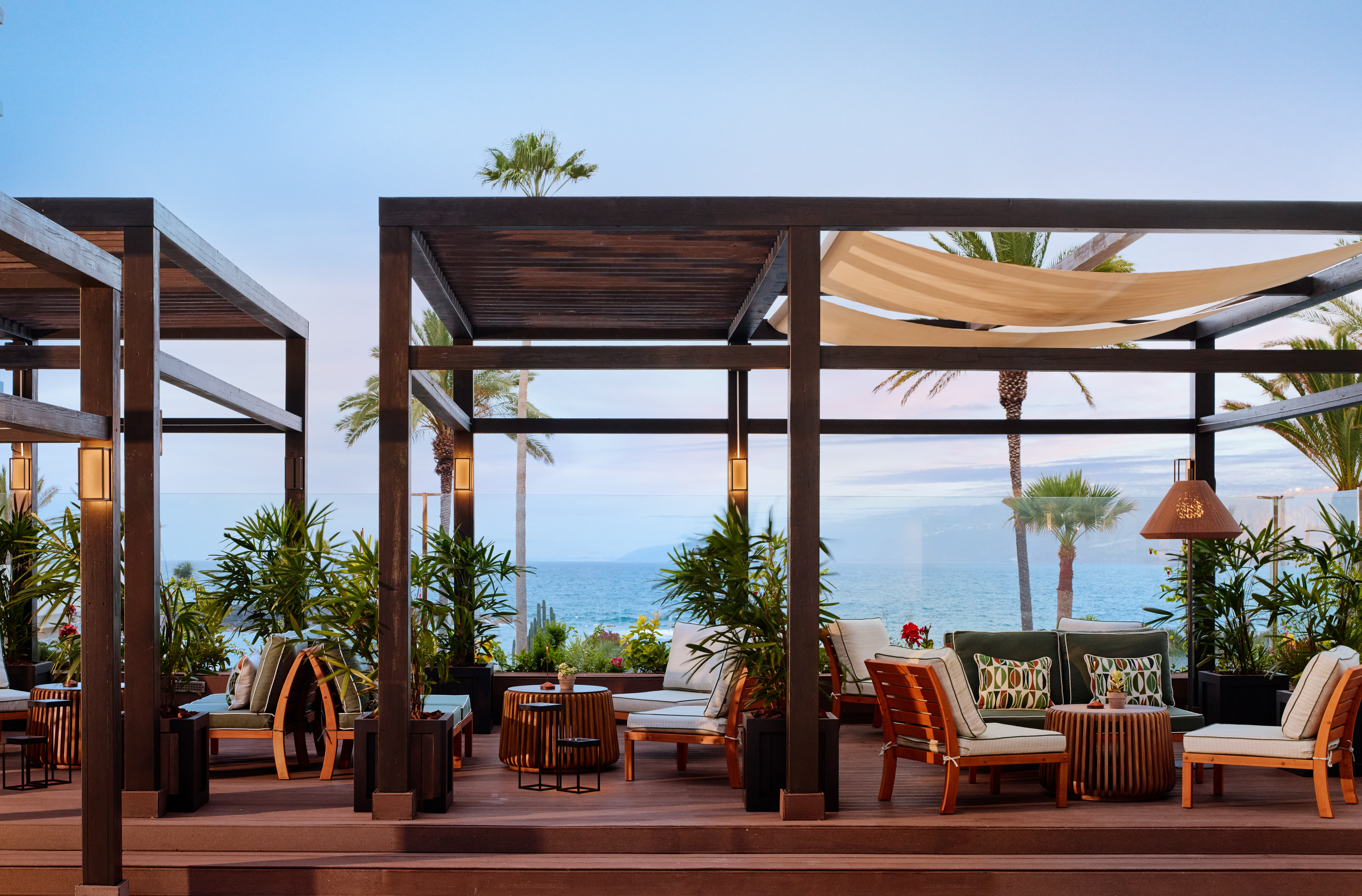 Luxury oceanfront lounge with pergolas, tropical plants, and sea view.