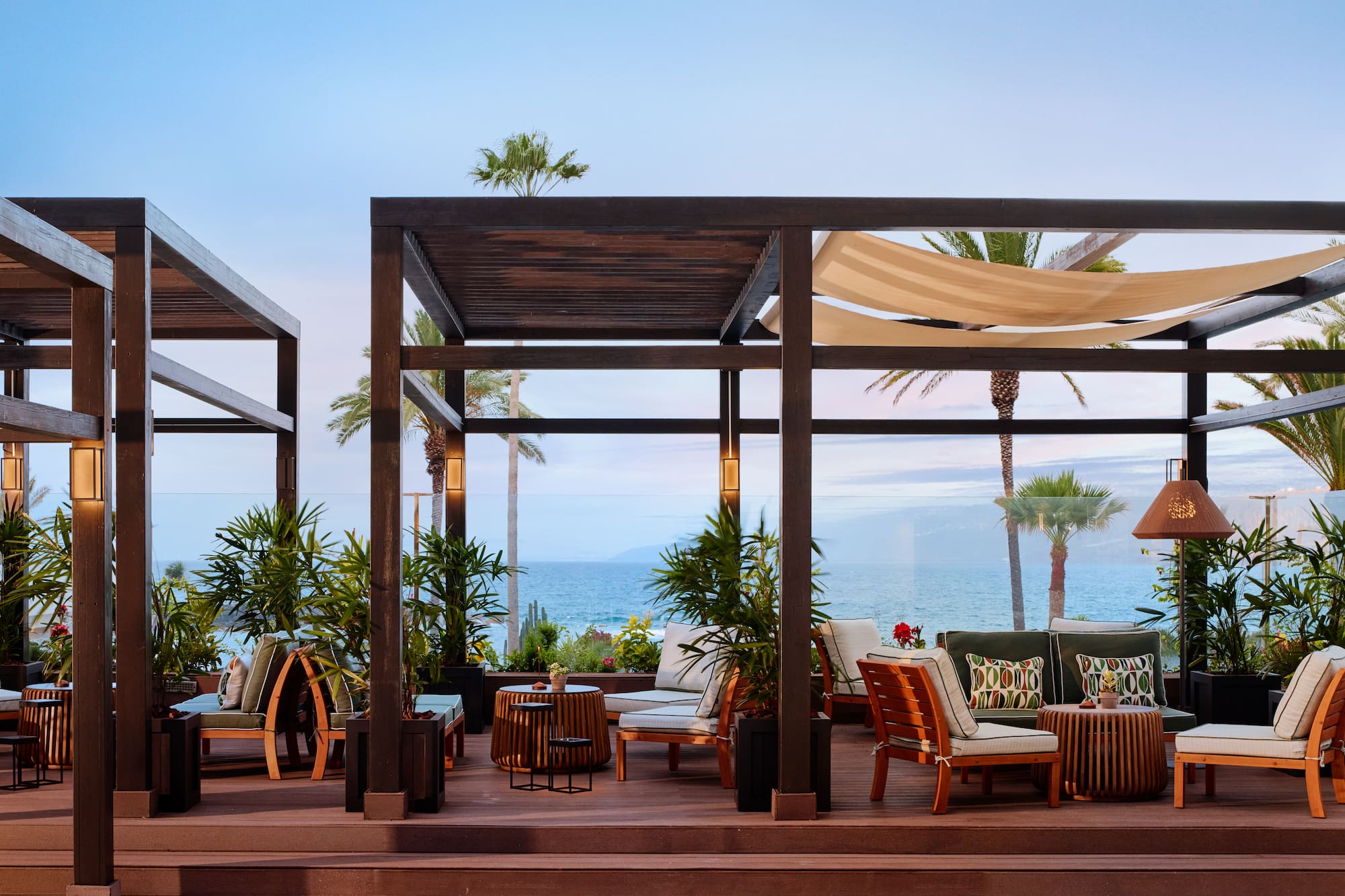 Luxury oceanfront lounge with pergolas, tropical plants, and sea view.