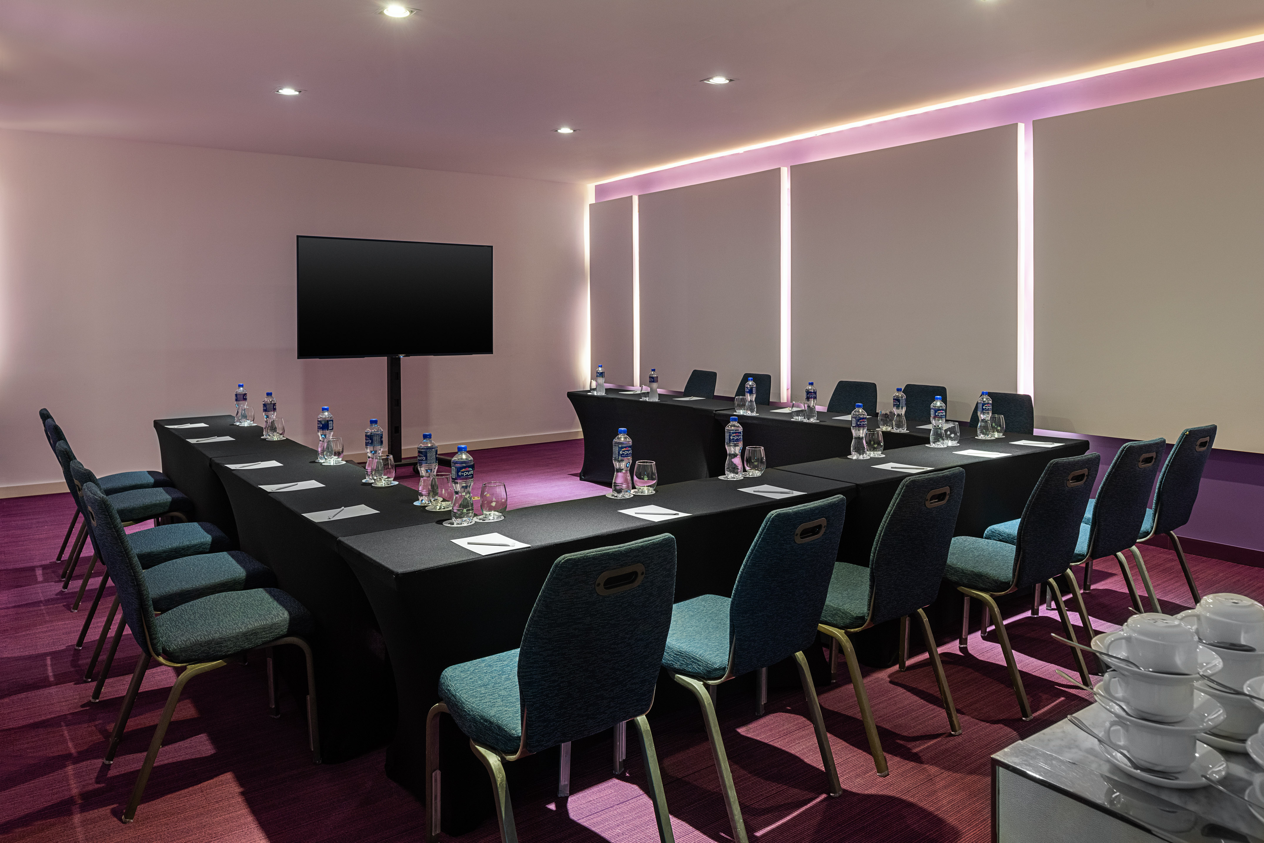 U-shaped modern meeting room with teal chairs, black tables, and TV.
