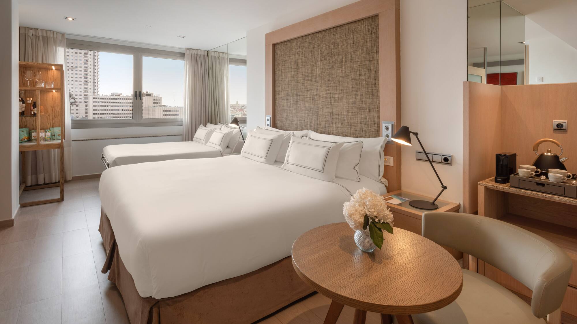 Modern hotel room with double bed, single bed, city view, and coffee station.