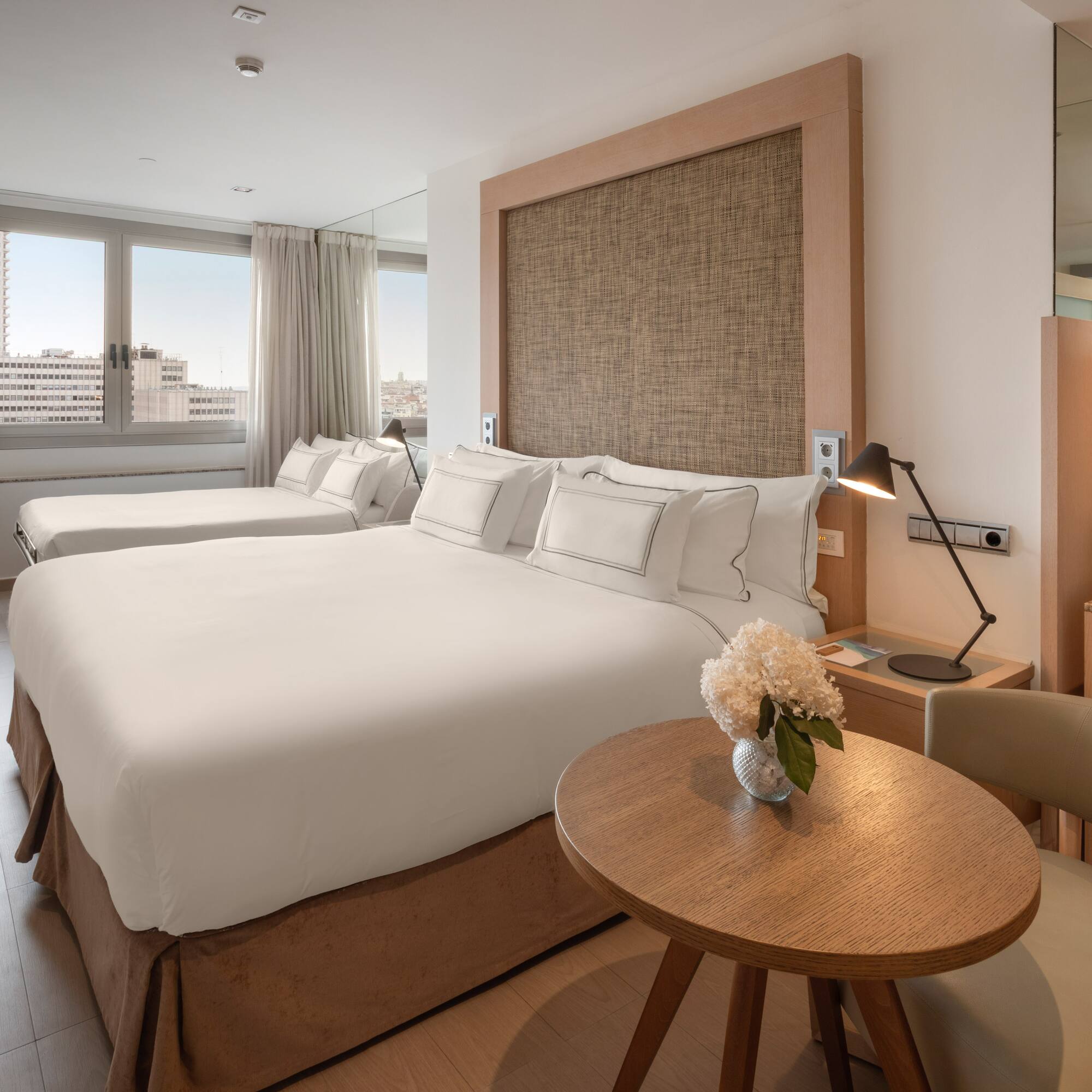 Modern hotel room with double bed, single bed, city view, and coffee station.