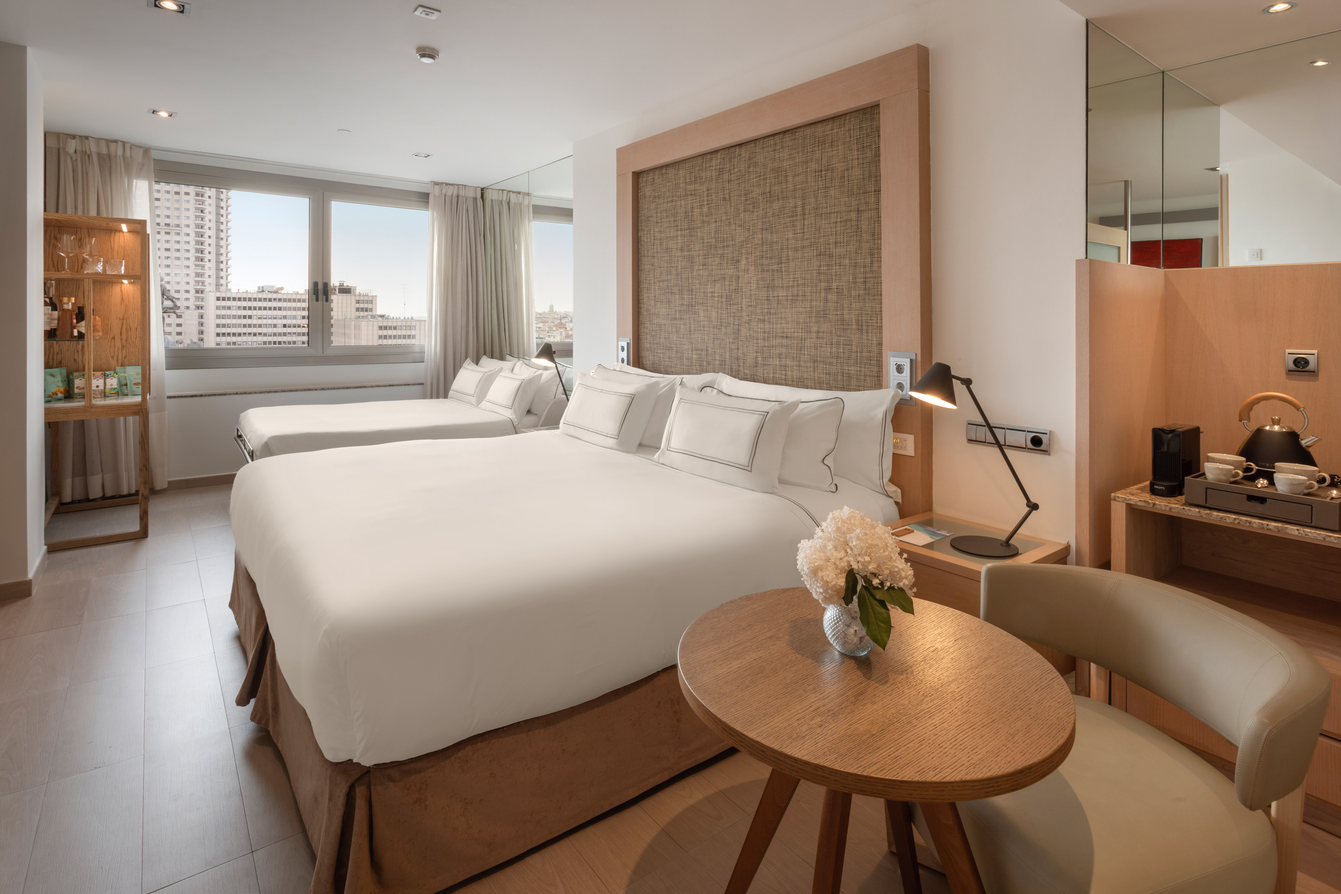 Modern hotel room with double bed, single bed, city view, and coffee station.