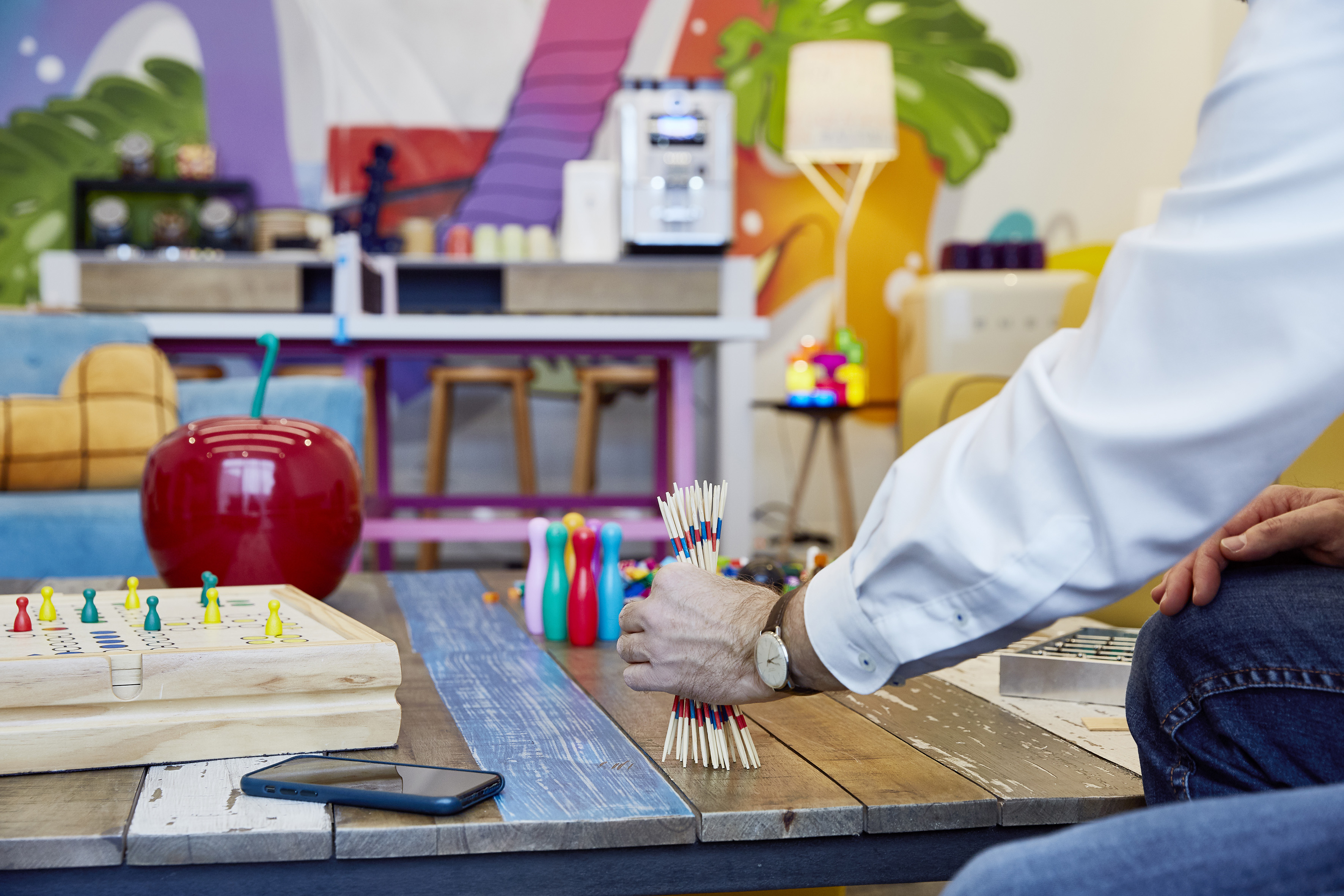 Hand holds Mikado sticks on wooden table with board game in colorful lounge.